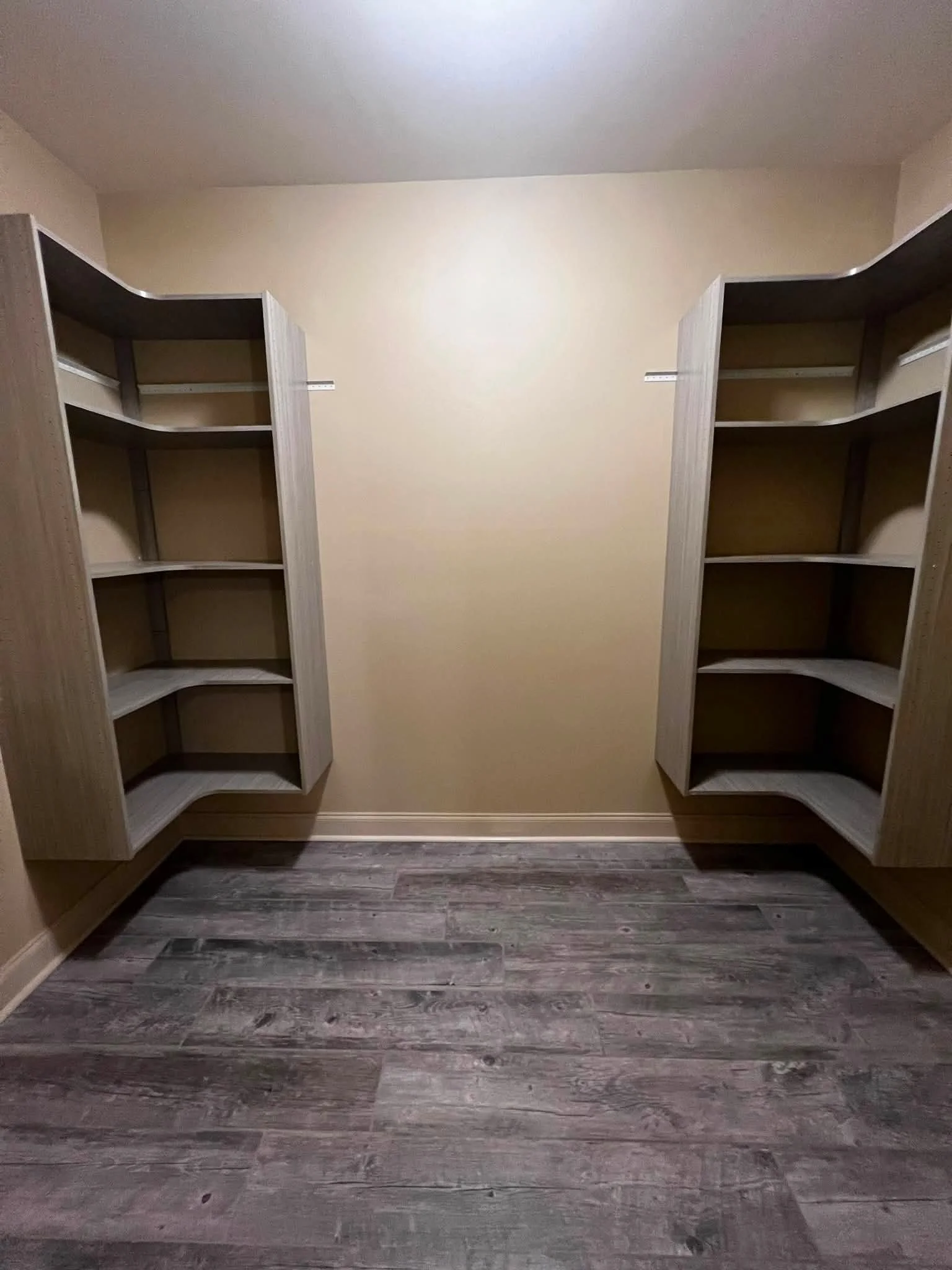 Empty walk-in closet with wooden shelves on each side and dark wood laminate flooring.