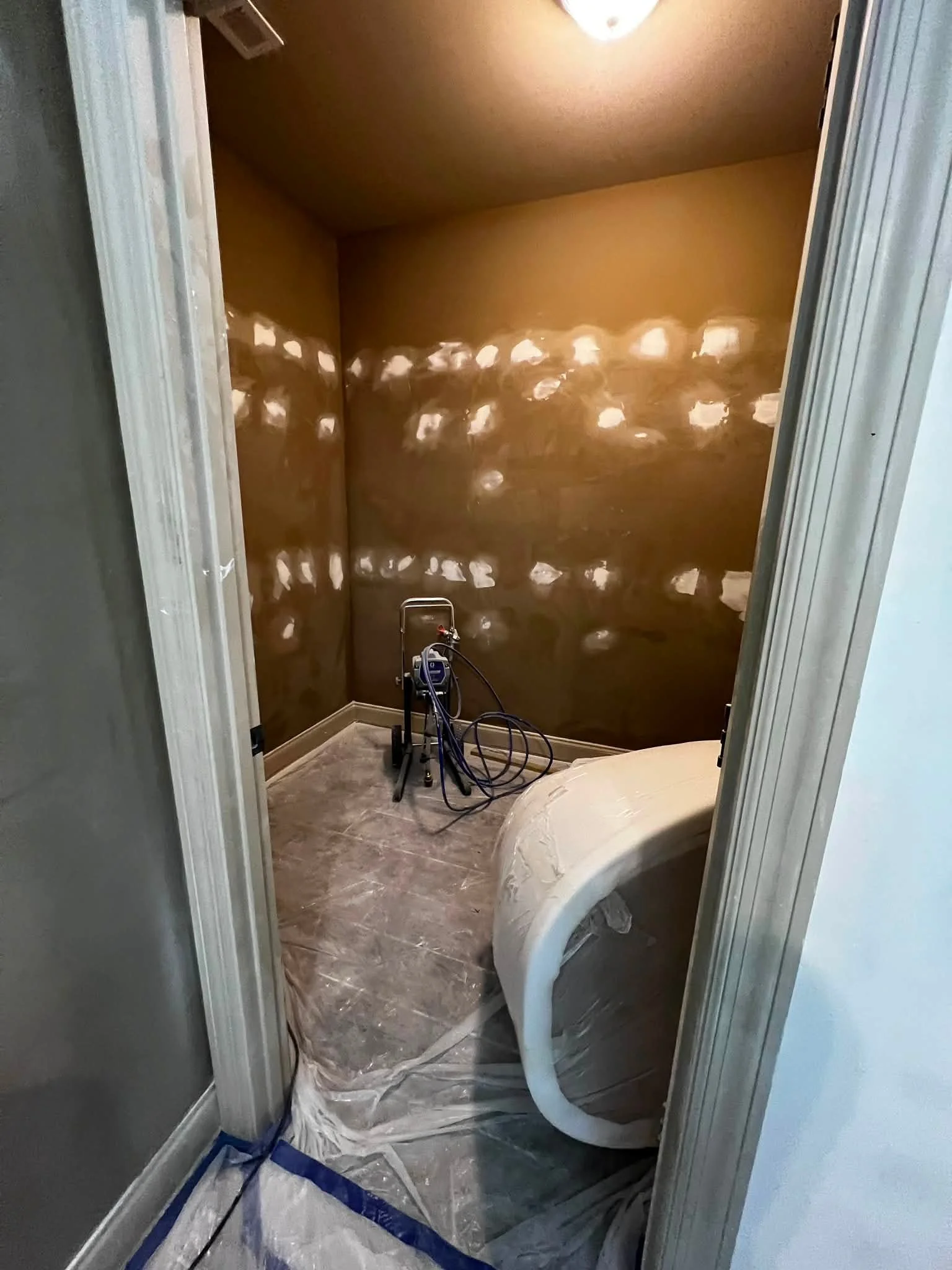 A small bathroom under renovation with a large bathtub, a plastic sheet on the dark gray marble floor, a painting sheet cover, a towel bar, and a plastic sheet protecting the door frame.