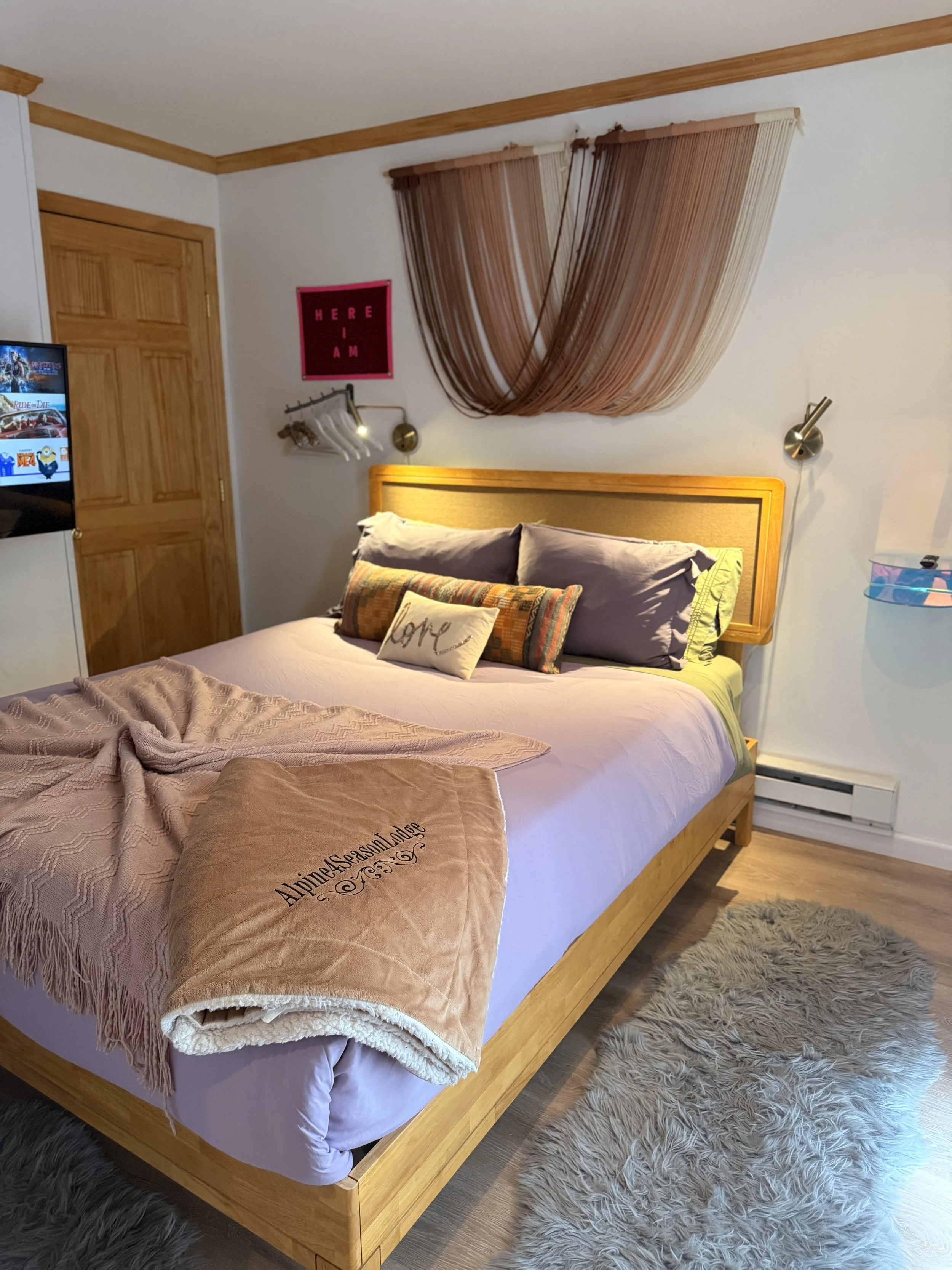   🛏️ Cozy bedroom at Alpine Four Season Lodge with a wooden bed, soft linens and warm lighting for a restful stay.