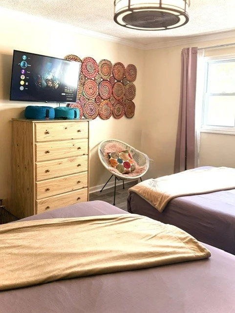Relax in a bright Catskills bedroom with two cozy queen beds, plush four-season bedding, Smart TV, and peaceful mountain charm perfect for restful getaways year-round.