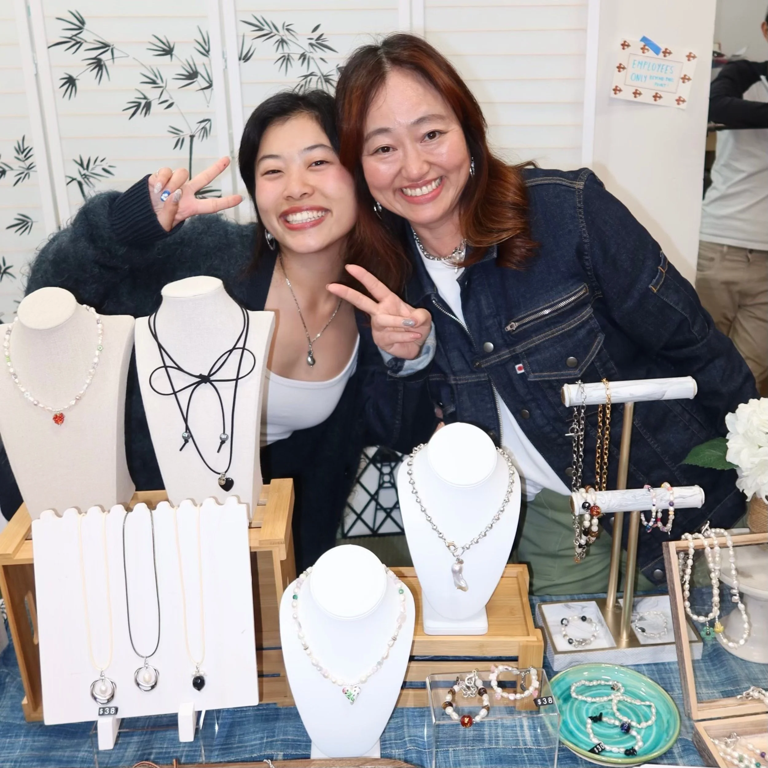 Two women smiling at a jewelry display booth with necklaces, bracelets, and earrings.
