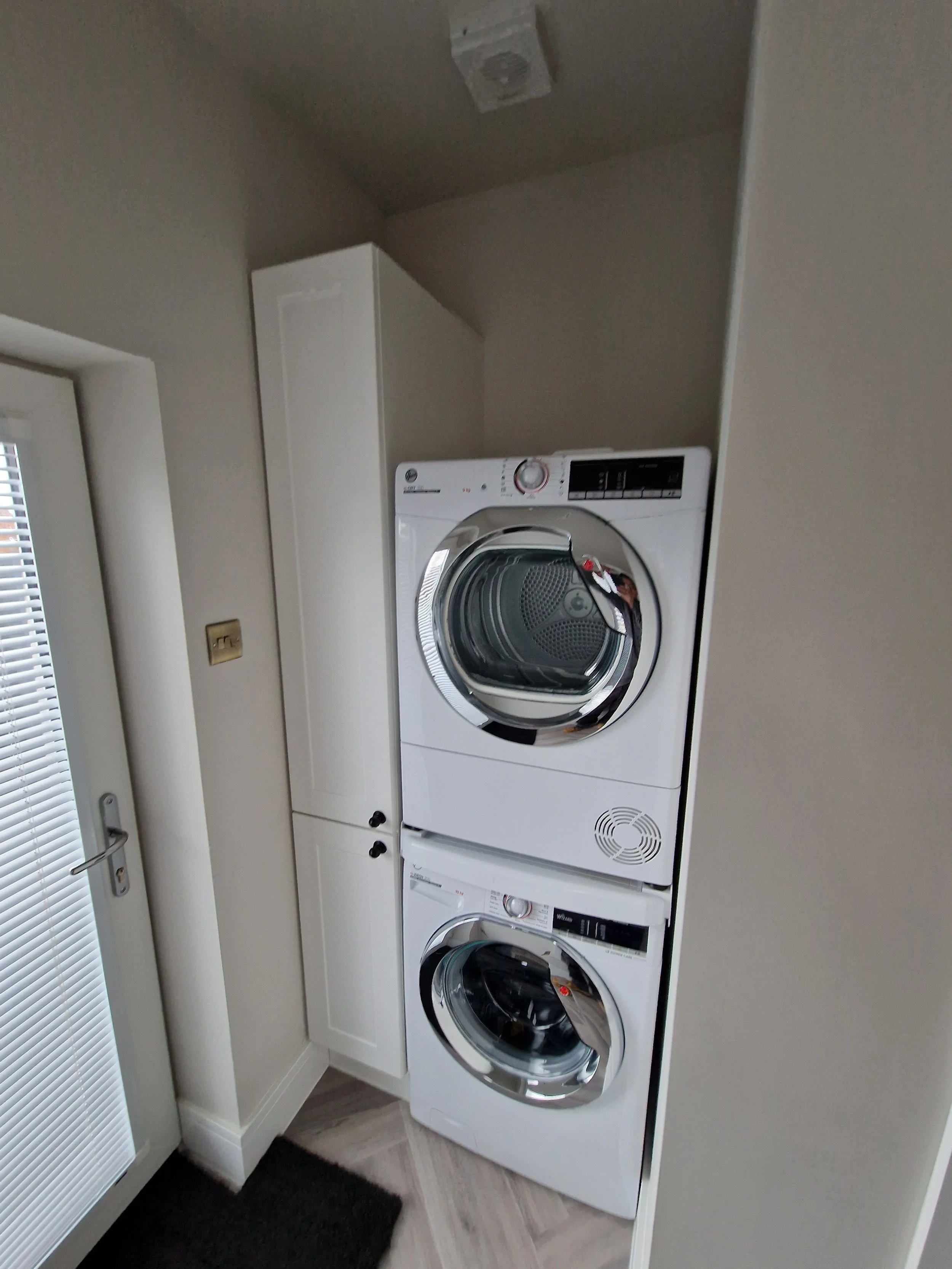 Stacked washing machine and dryer in a laundry room next to a tall white cabinet.