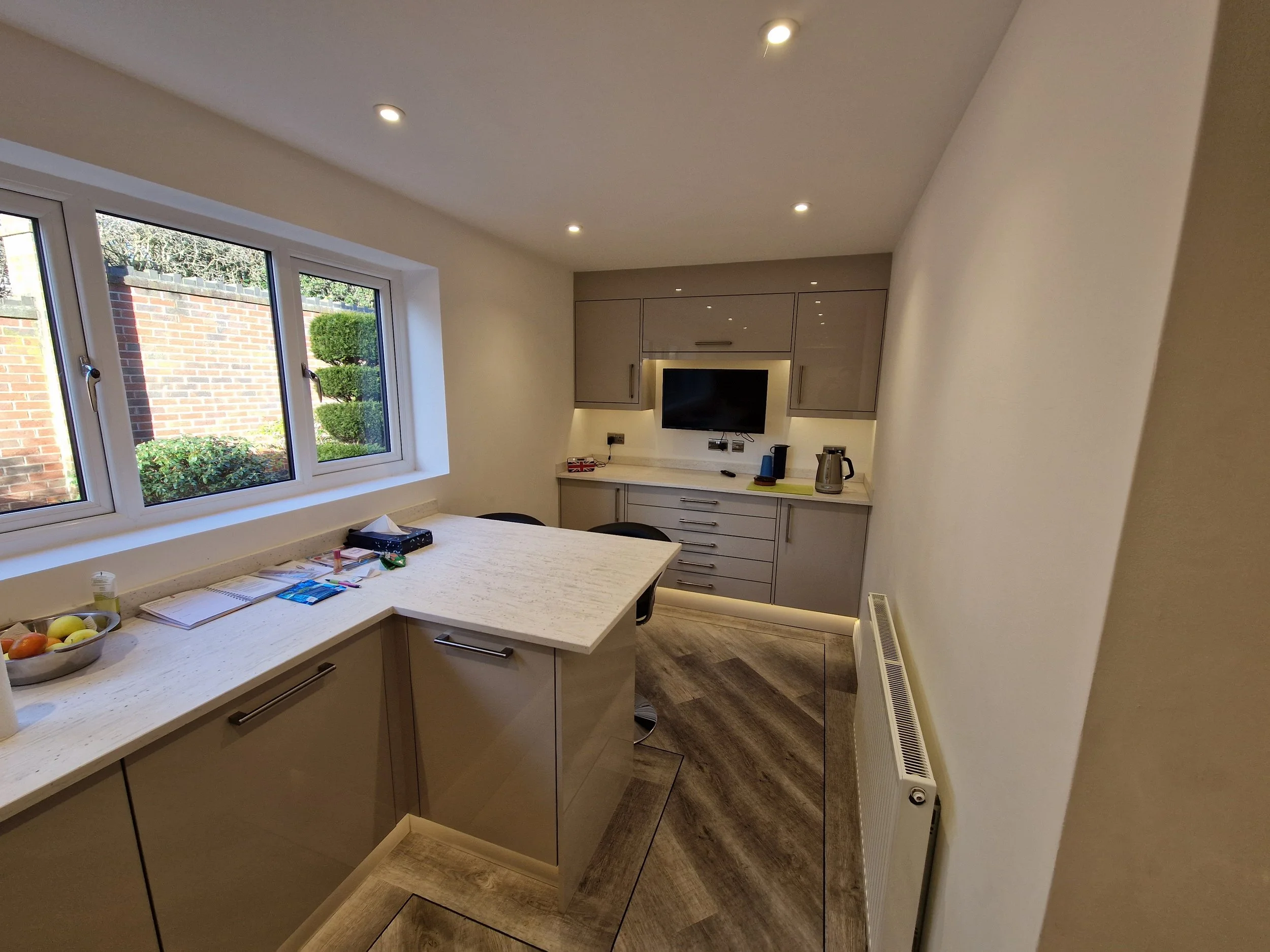 Modern kitchen with grey cabinets, a white marble countertop, a window overlooking a garden, and a small dining table with chairs.