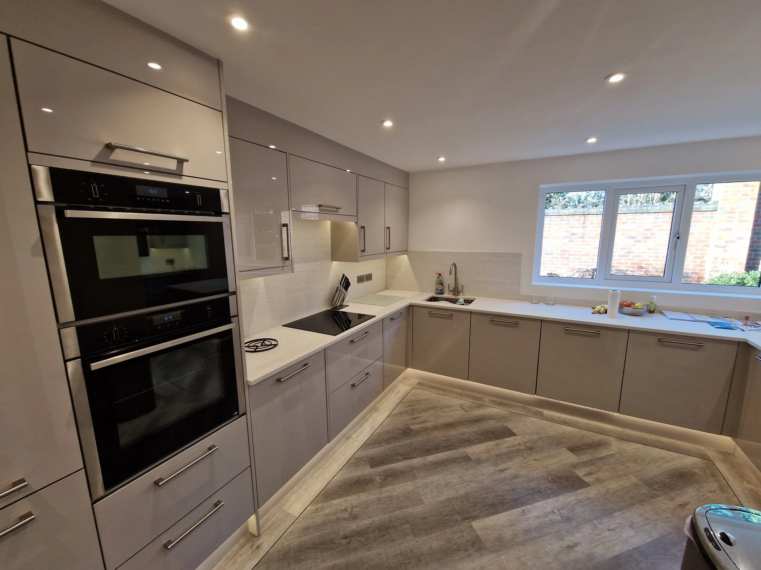 Modern kitchen with gray cabinets, white countertops, a window overlooking a brick wall, and built-in oven and cooktop.