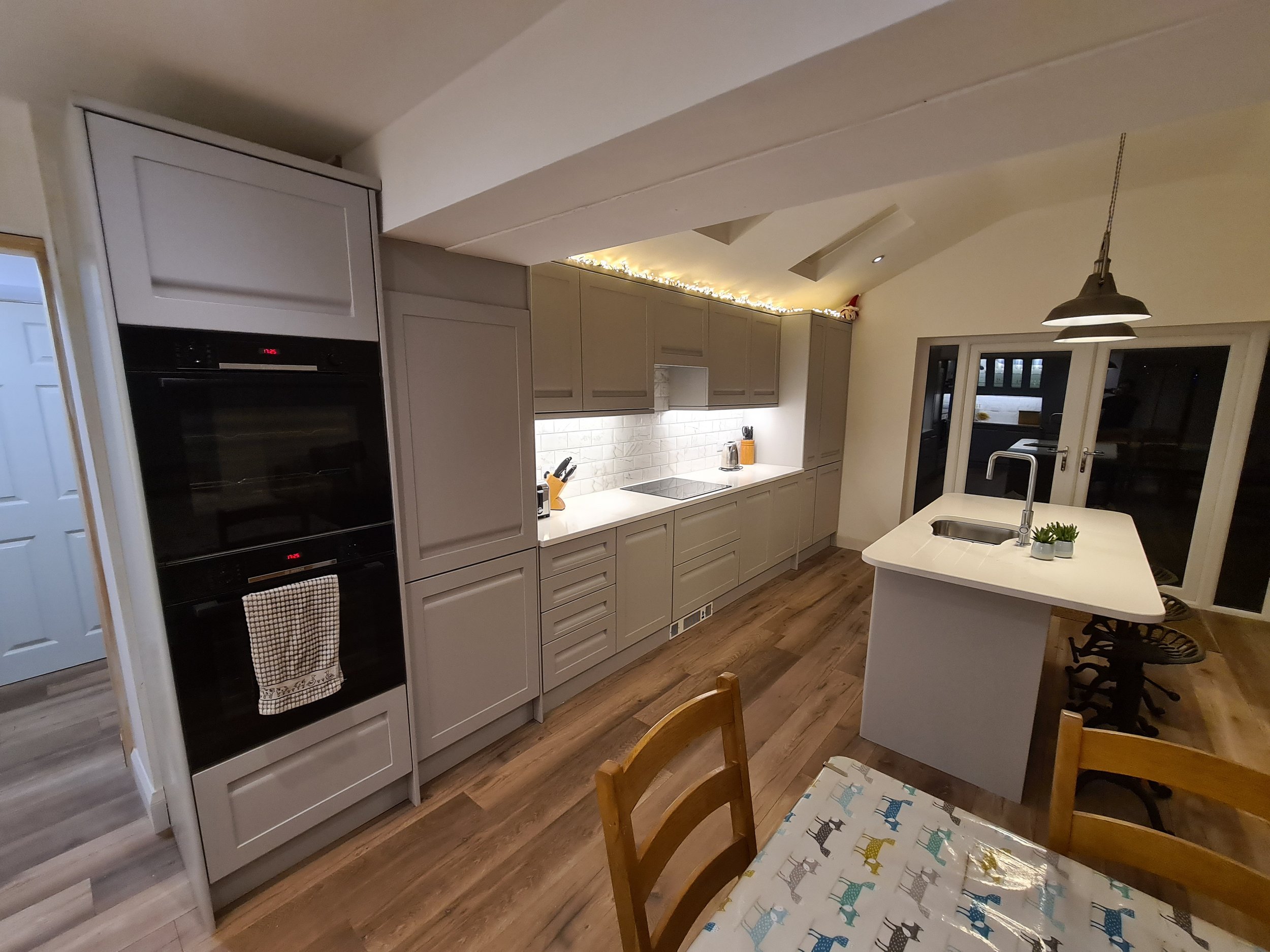 Modern kitchen with white cabinetry, wood flooring, and a kitchen island with a sink, overlooking sliding glass doors.