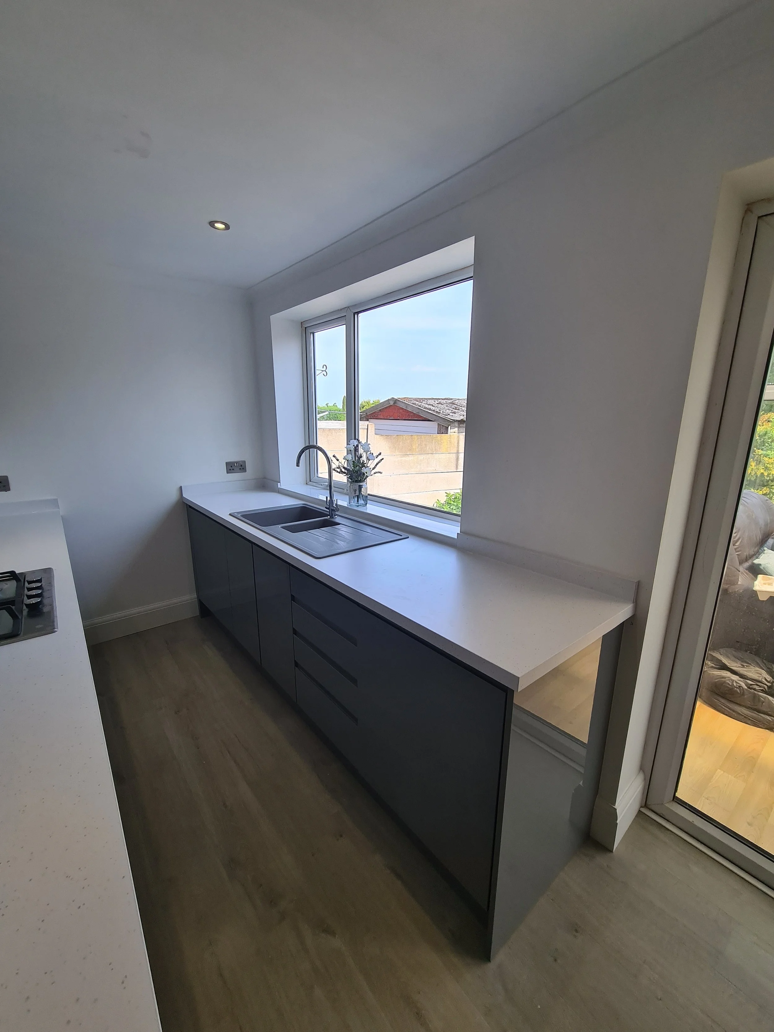 Modern kitchen with white countertops, dark gray cabinets, a window above the sink, and a sliding glass door on the right.