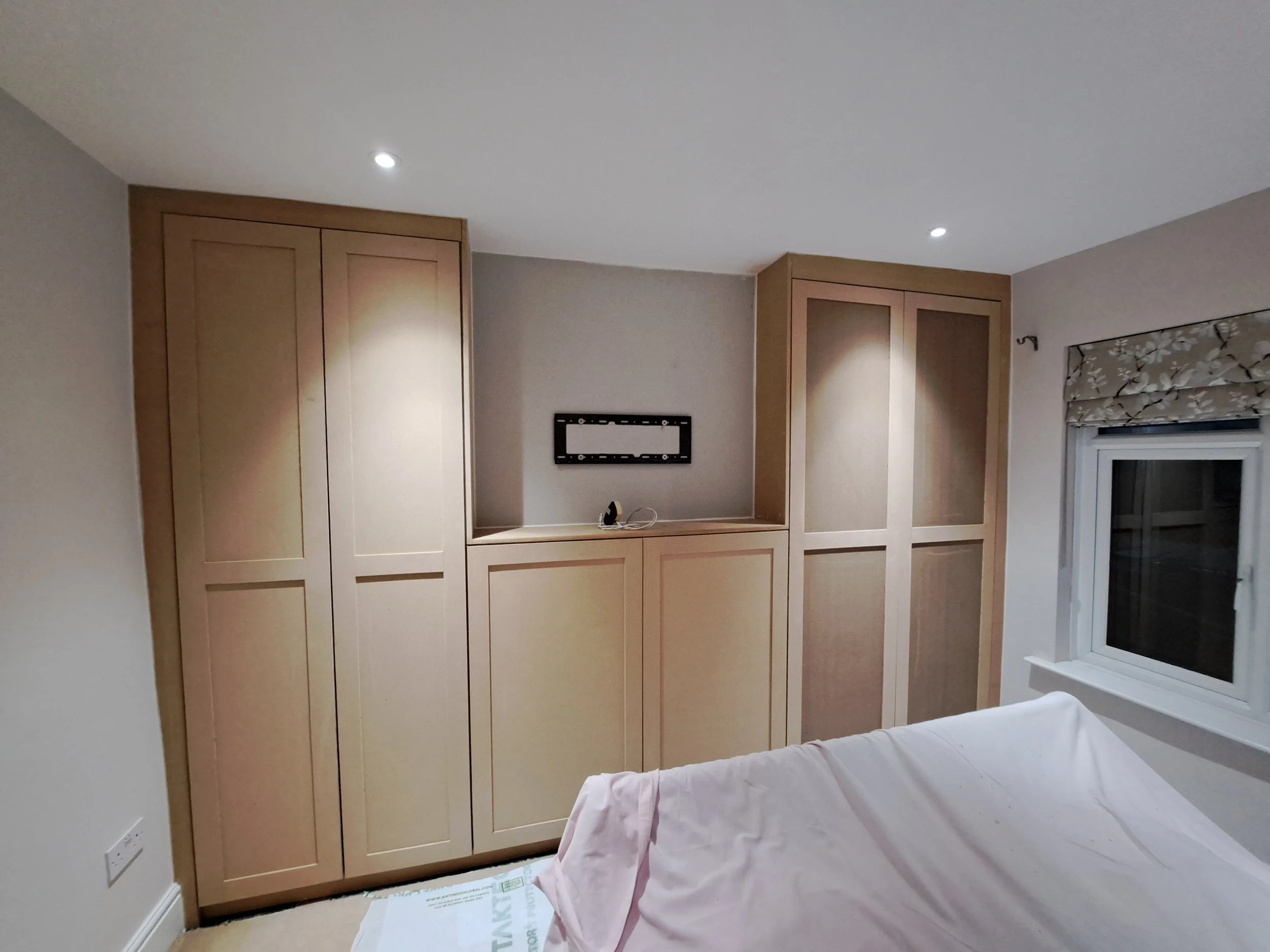 Room with built-in wooden wardrobes, a window with floral curtain, and a covered bed.