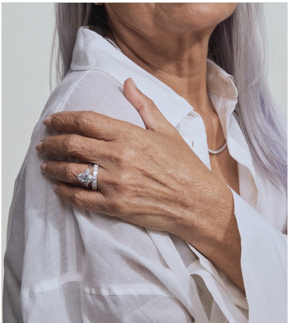 A woman wears a white blouse and holds a bejeweled hand on her shoulder