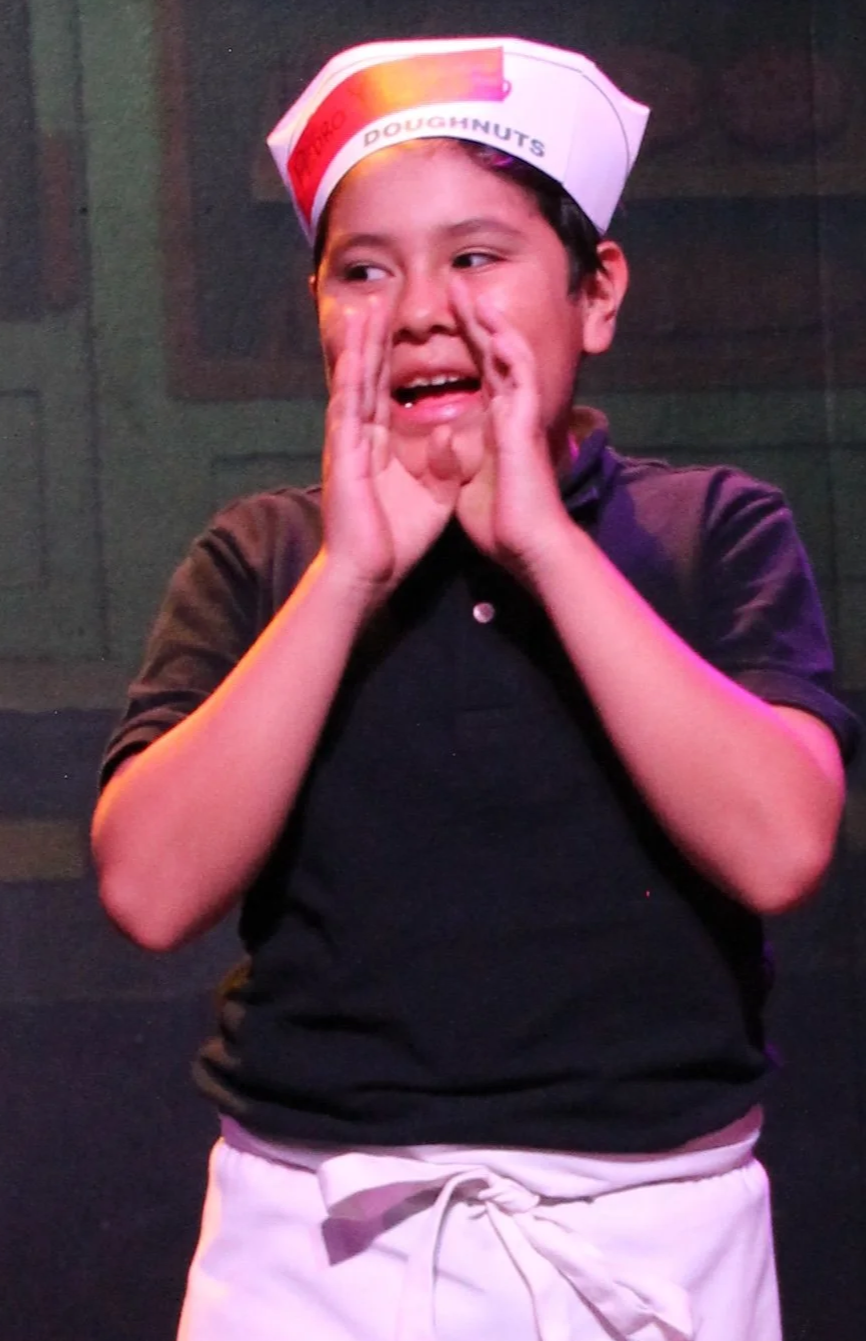 A photo of a young boy wearing a paper hat and apron in order to play a baker in a play.