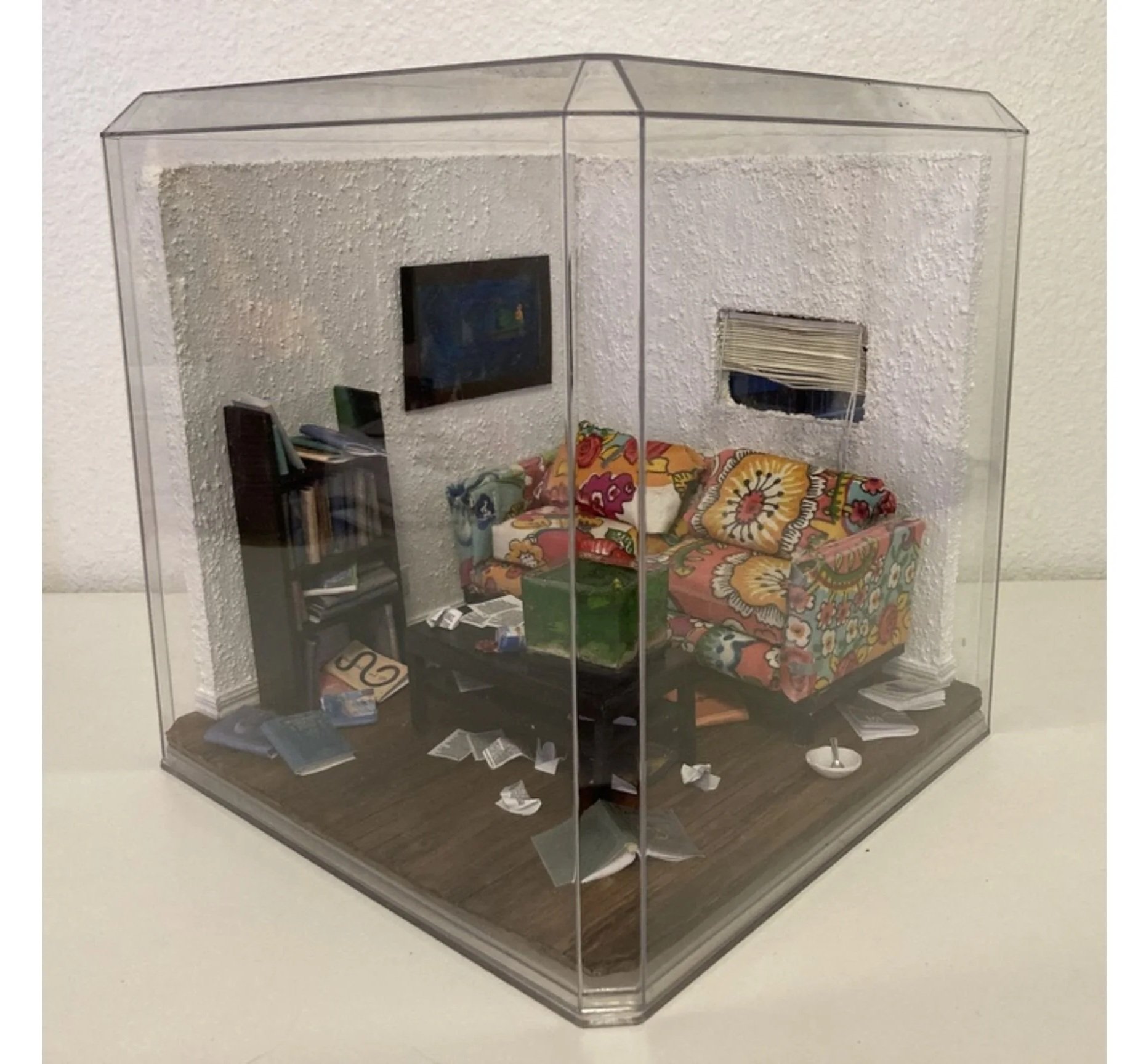 Miniature room of a messy room with a couch, bookshelf, and window.