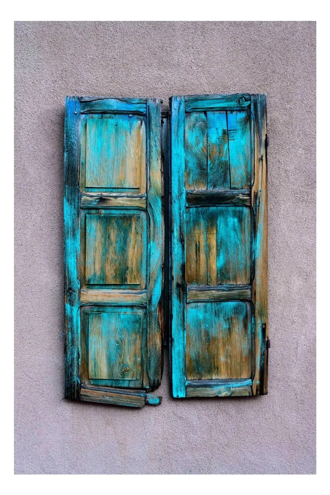 A pair of weathered, turquoise-painted wooden shutters mounted on a textured gray wall.