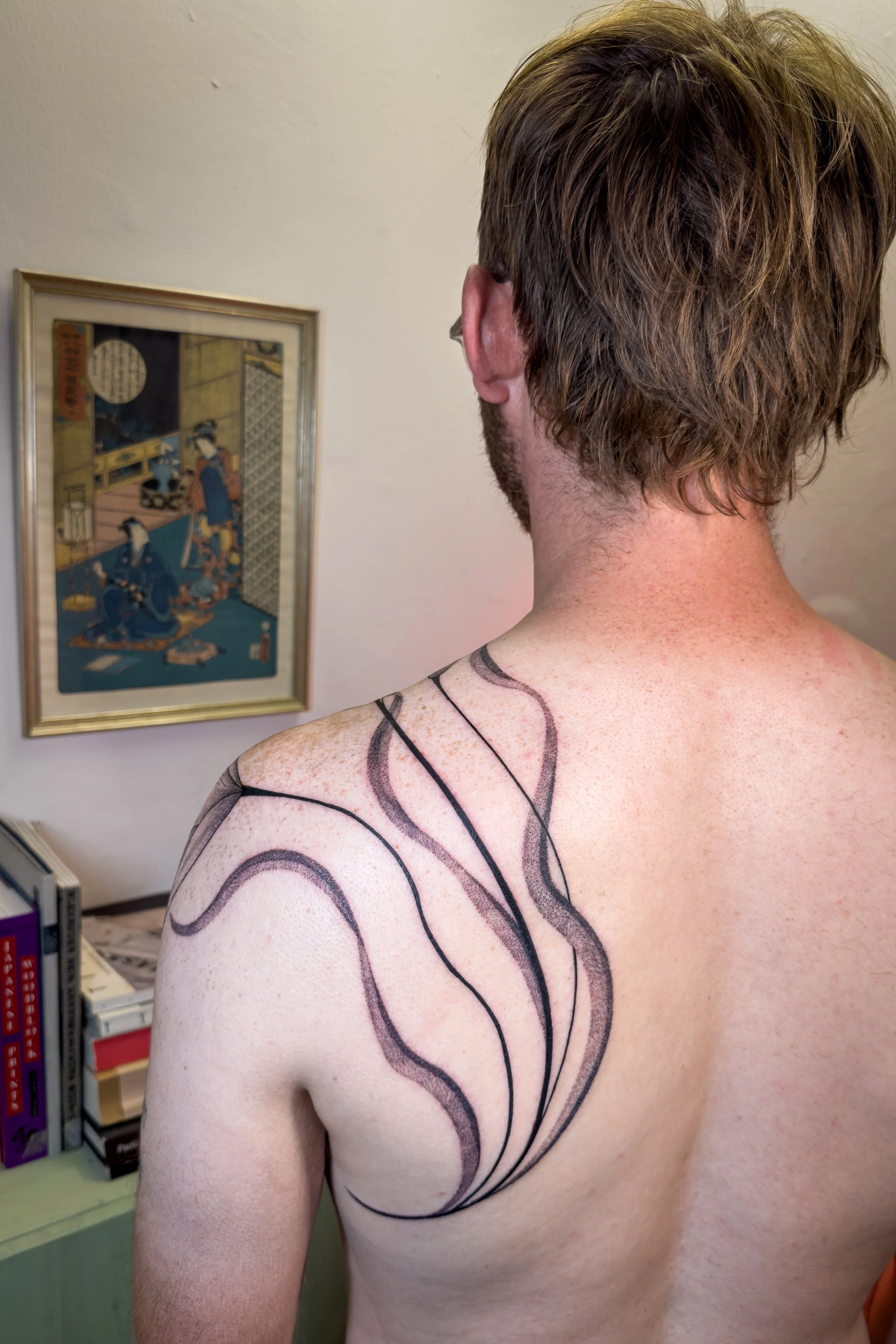 Freehand shoulder and back tattoo by Lis Roldan, featuring lily flowers, custom-designed to follow the natural movement and anatomy of the body, creating a fluid and harmonious composition that flows seamlessly with the form.