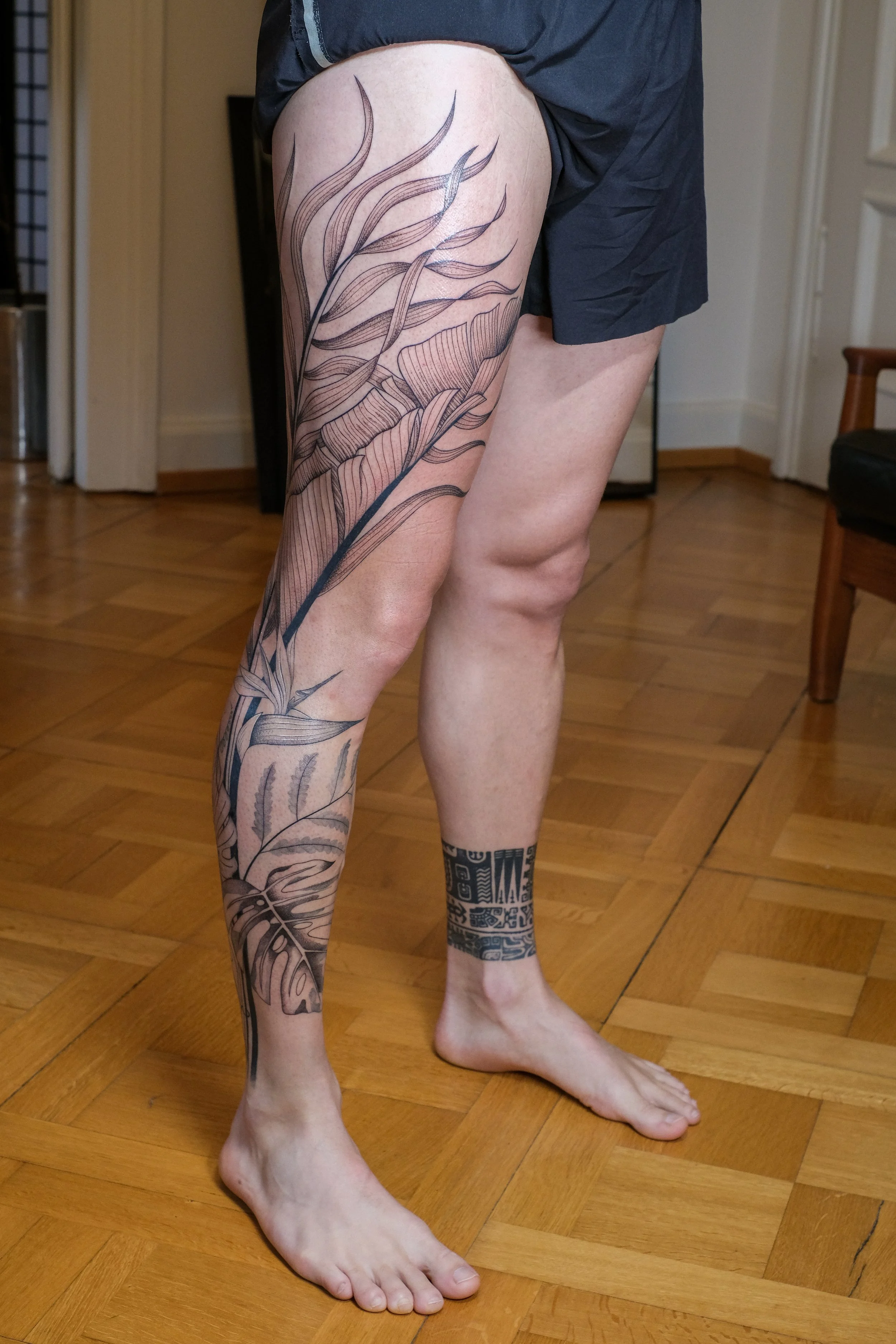 Freehand botanical leg tattoo by Lis Roldan, featuring tropical flowers and plants, custom-designed to follow the natural movement and anatomy of the leg, creating a fluid and harmonious composition.