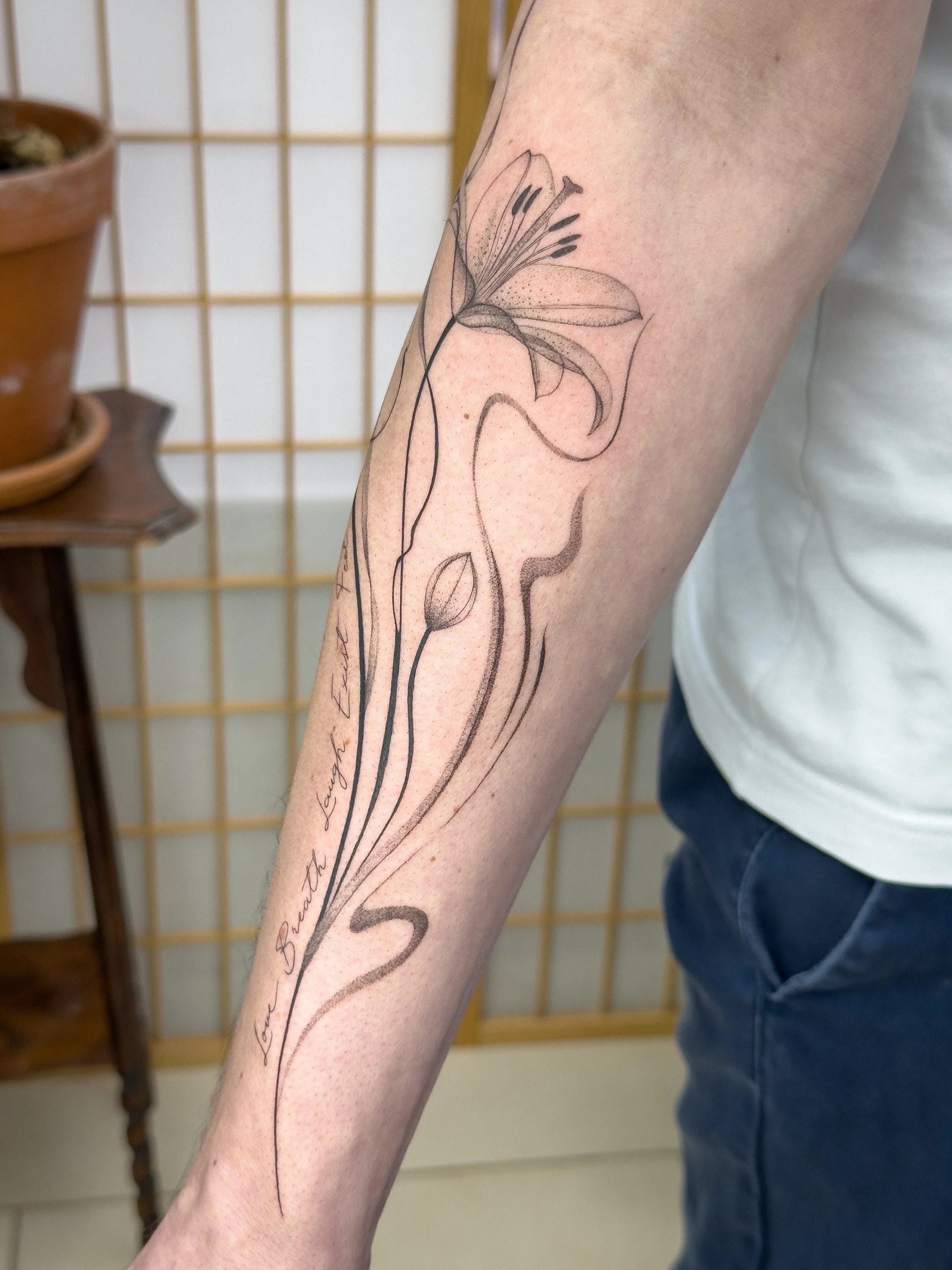 Custom fine line lily tattoo designed and created by Lis Roldan. Flowing lines and soft shading follow the natural shape of the forearm, creating a minimal and harmonious composition.