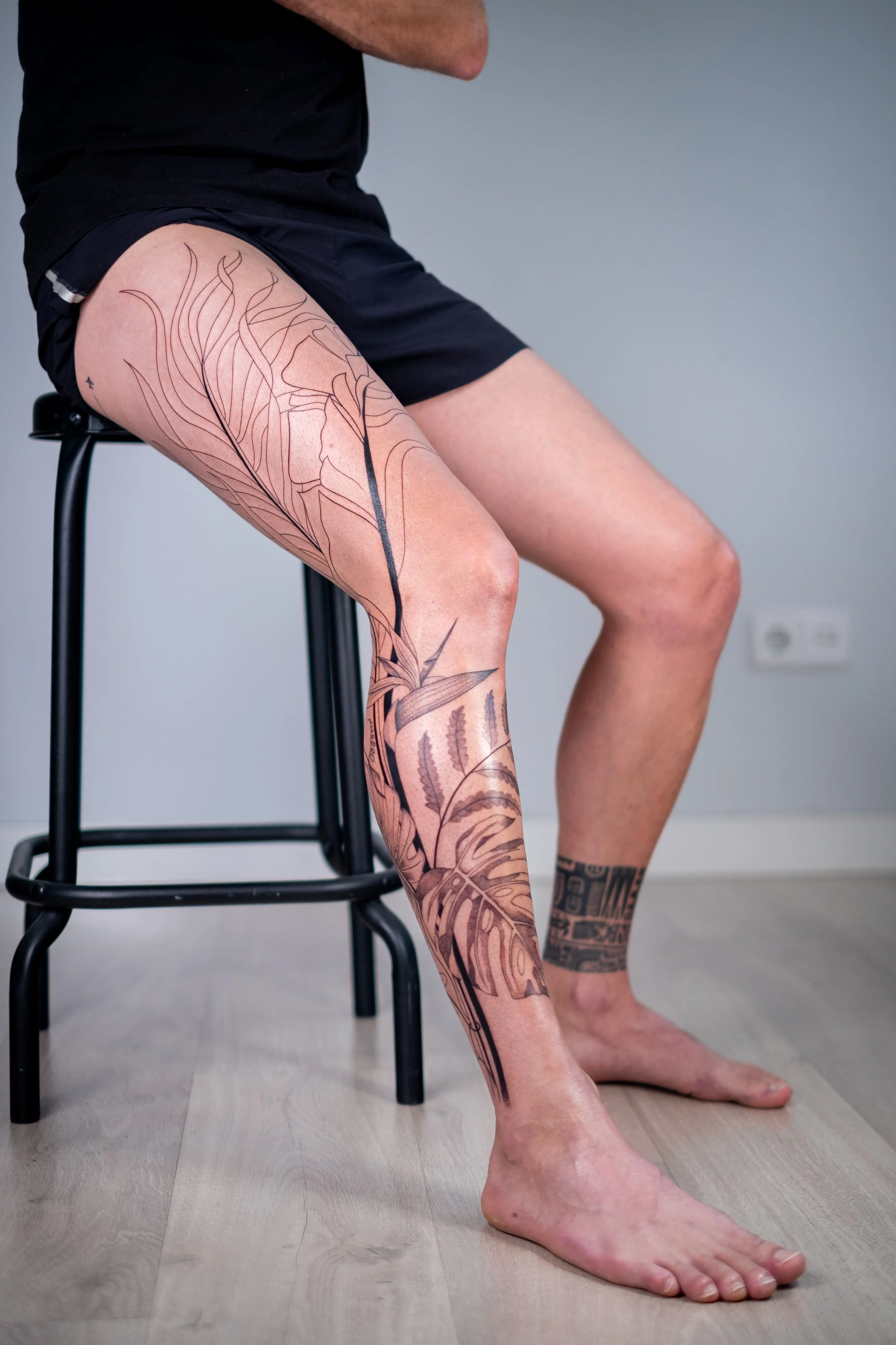 Freehand botanical leg tattoo by Lis Roldan, featuring tropical flowers and plants, custom-designed to follow the natural movement and anatomy of the leg, creating a fluid and harmonious composition.