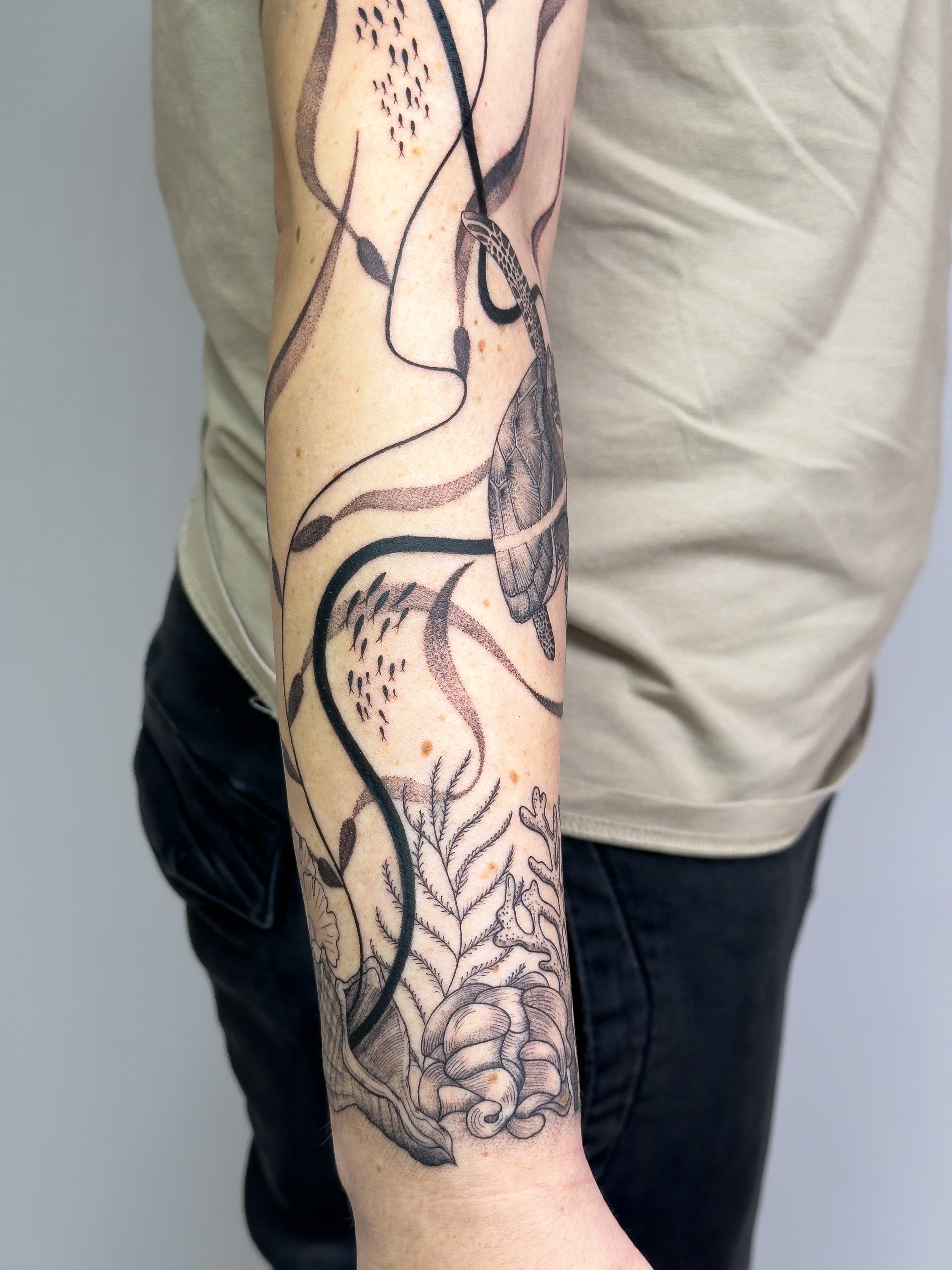 Sea-inspired arm tattoo featuring flowing freehand lines, botanical elements, and a sea turtle, tattooed by Lis Roldan over two sessions. This custom piece was designed to follow the natural shapes and movement of the arm, creating a harmonious and o