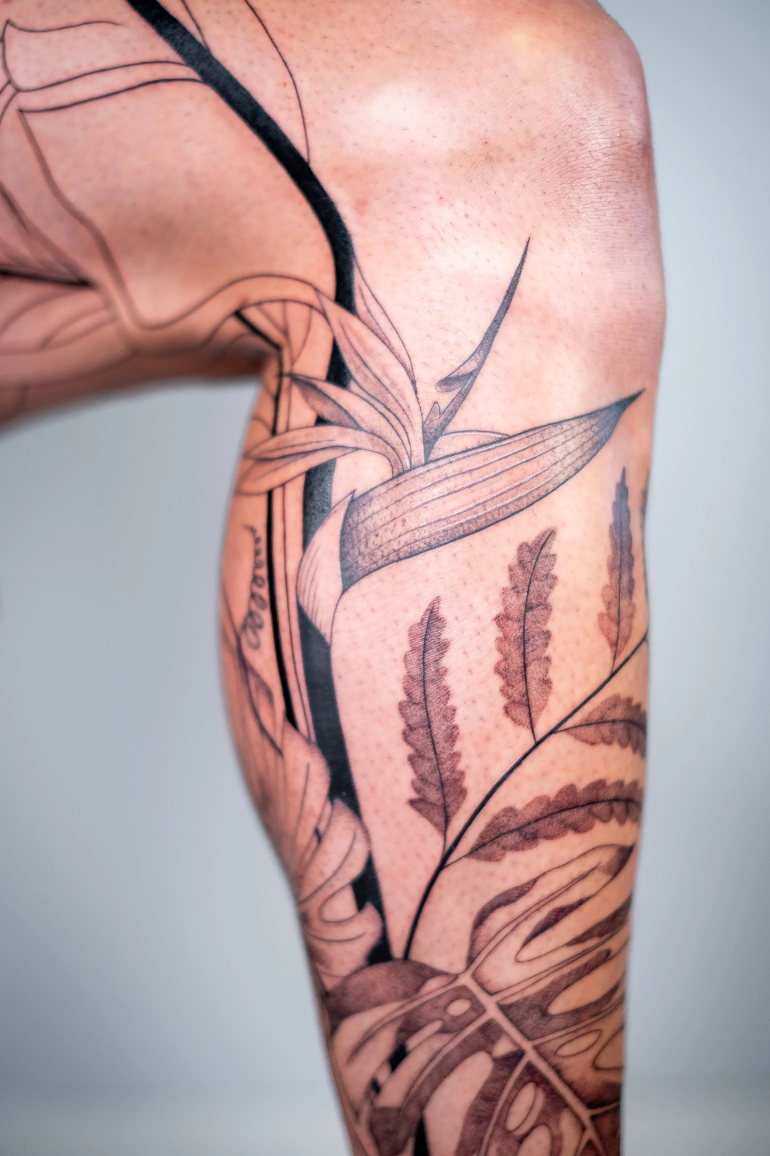 Freehand botanical leg tattoo by Lis Roldan, featuring tropical flowers and plants, custom-designed to follow the natural movement and anatomy of the leg, creating a fluid and harmonious composition.