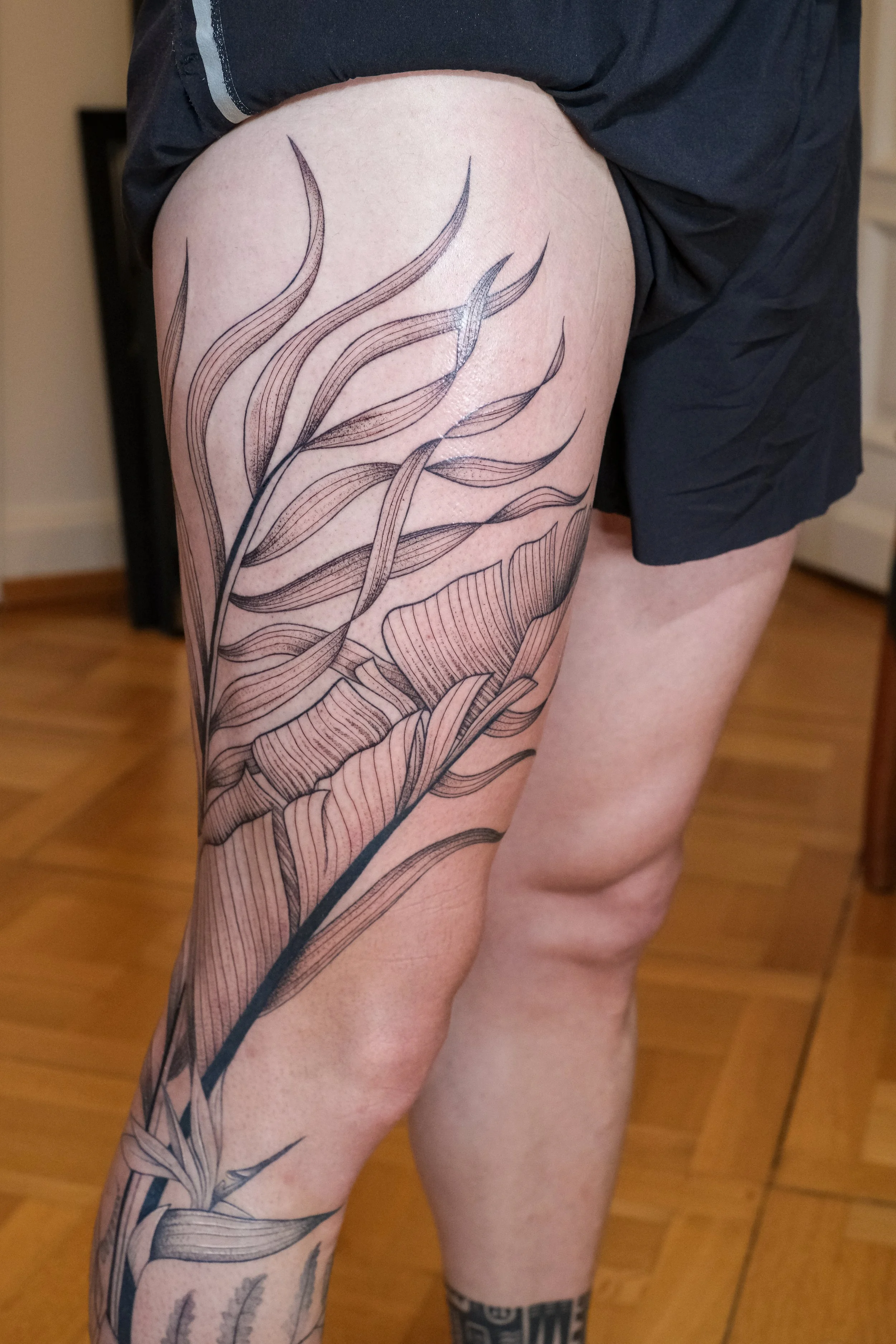 Freehand botanical leg tattoo by Lis Roldan, featuring tropical flowers and plants, custom-designed to follow the natural movement and anatomy of the leg, creating a fluid and harmonious composition.