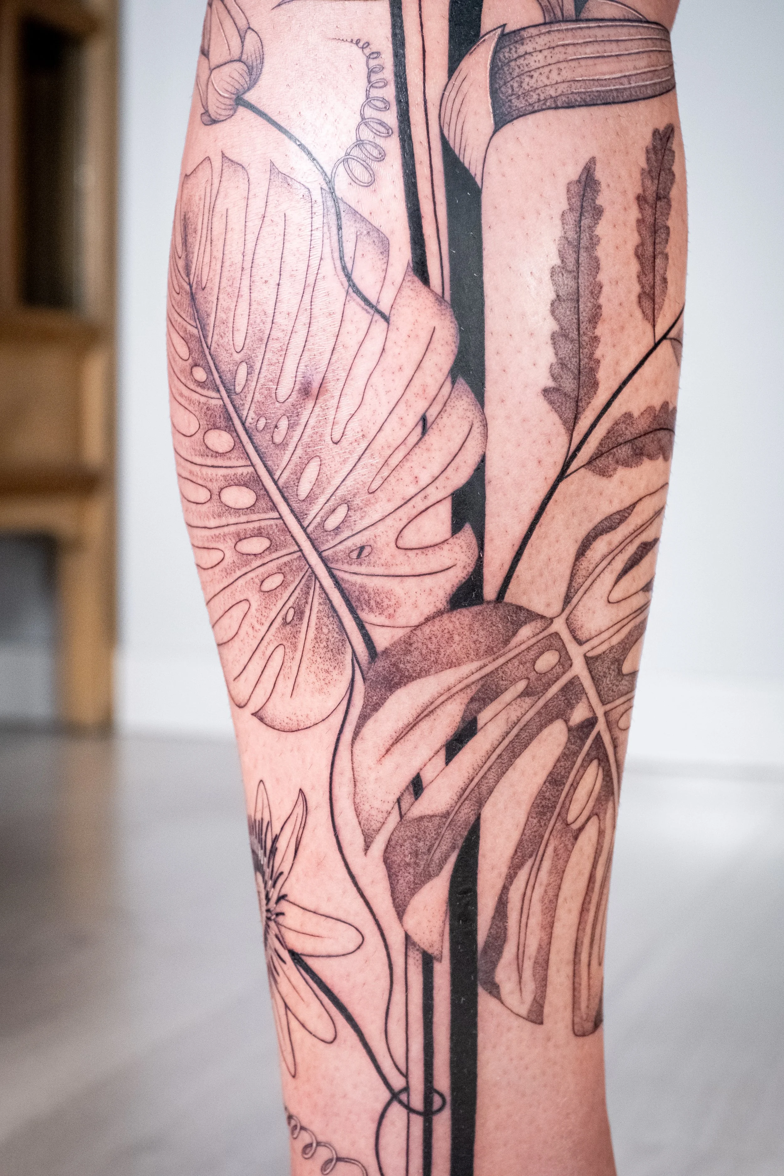 Freehand botanical leg tattoo by Lis Roldan, featuring tropical flowers and plants, custom-designed to follow the natural movement and anatomy of the leg, creating a fluid and harmonious composition.