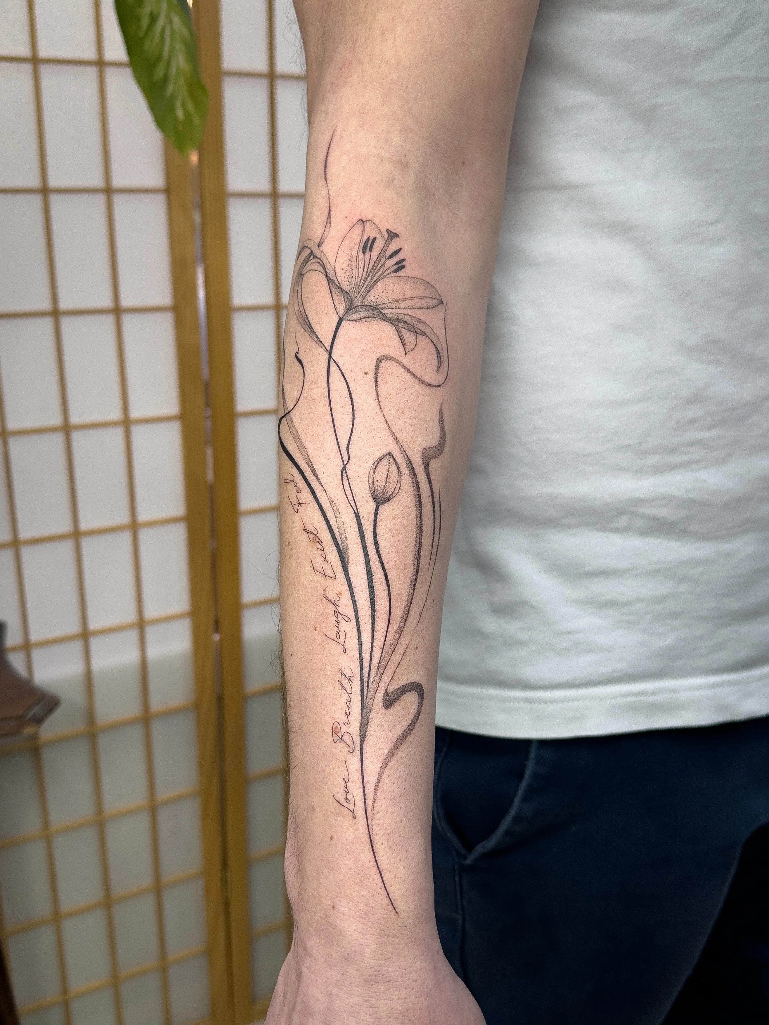 Custom fine line lily tattoo designed and created by Lis Roldan. Flowing lines and soft shading follow the natural shape of the forearm, creating a minimal and harmonious composition.