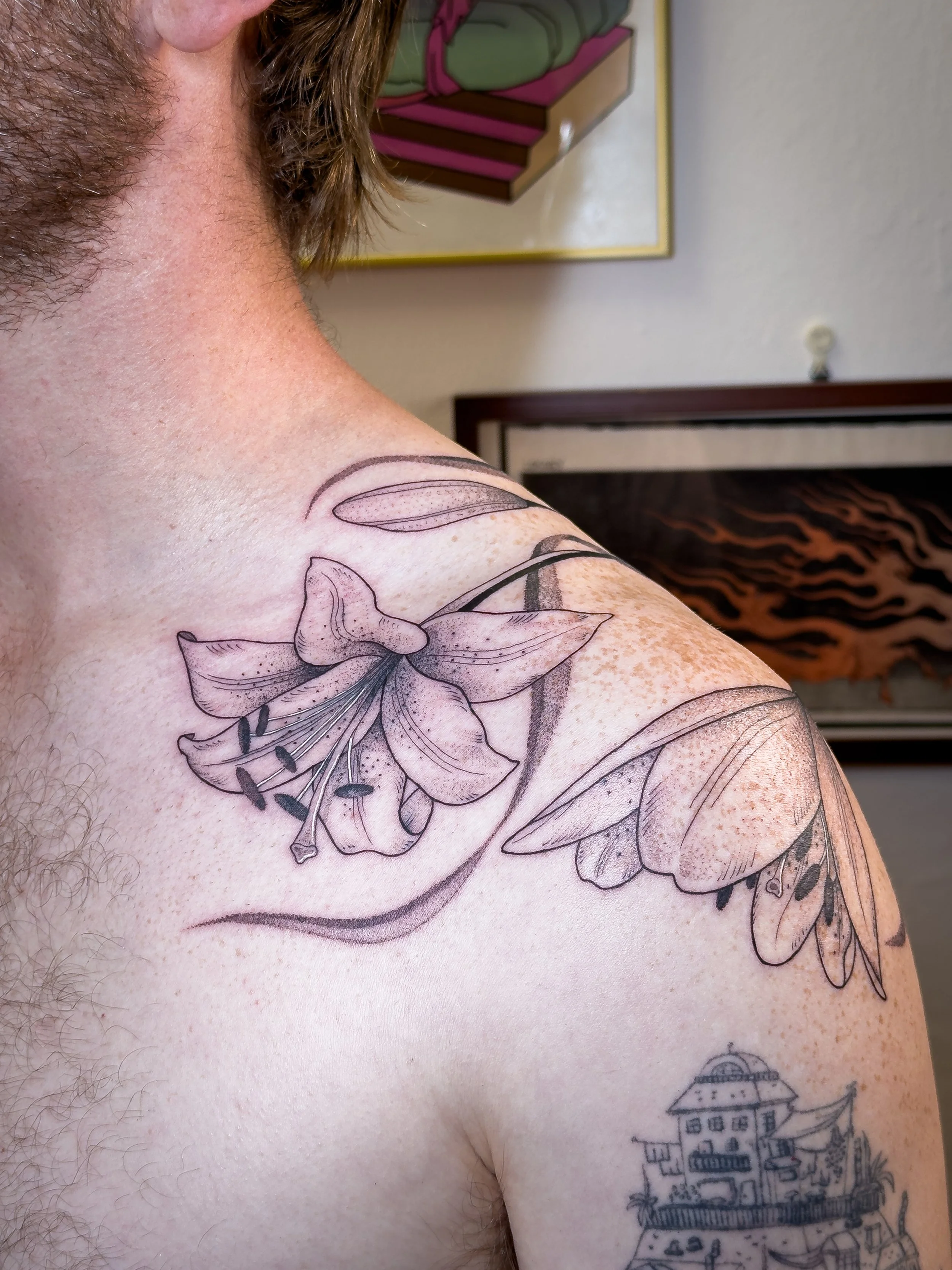 Freehand shoulder and back tattoo by Lis Roldan, featuring lily flowers, custom-designed to follow the natural movement and anatomy of the body, creating a fluid and harmonious composition that flows seamlessly with the form.
