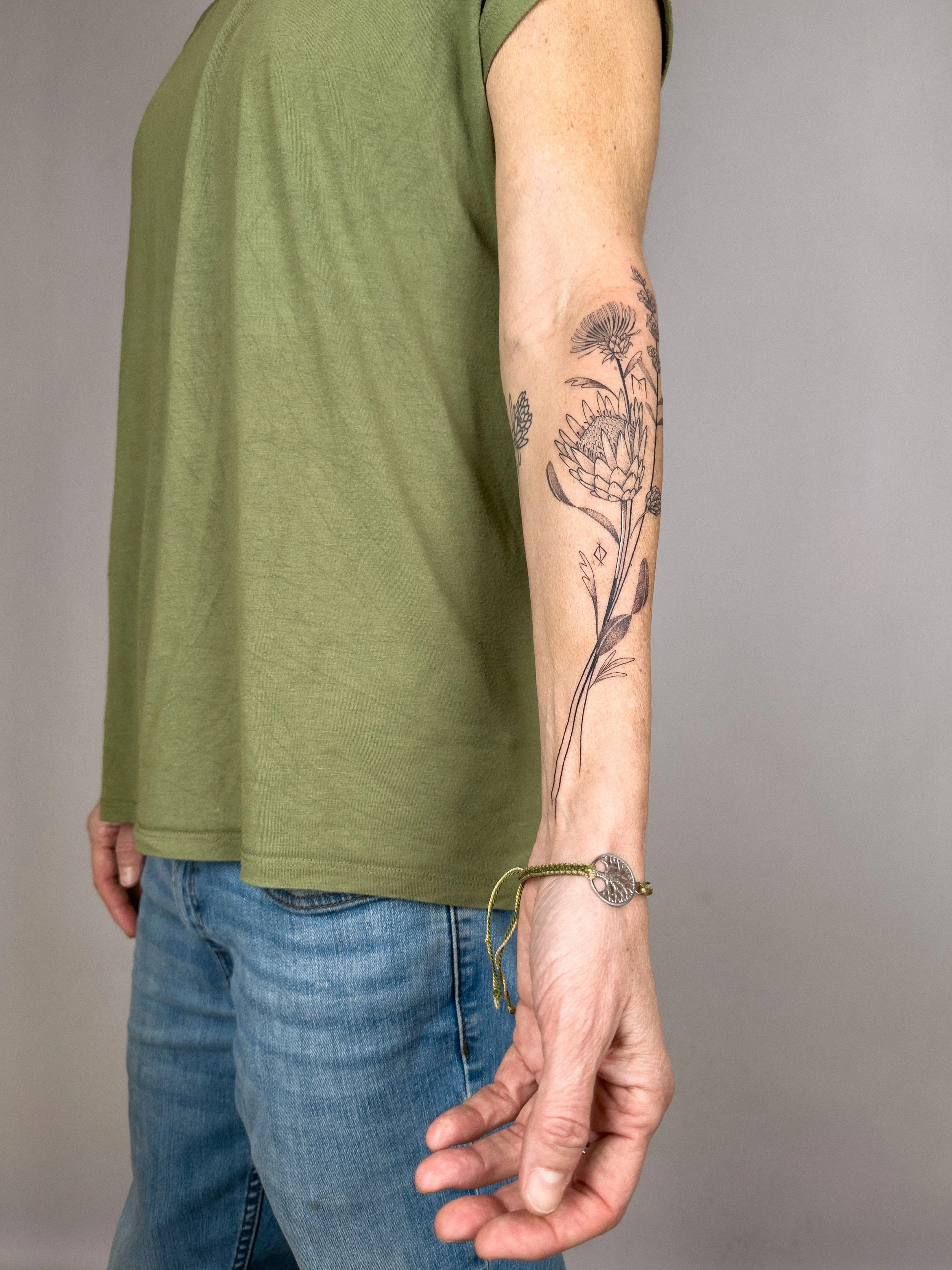 Fine line botanical tattoo featuring protea and thistle flowers, designed to flow naturally along the forearm. Soft shading and organic lines create a delicate and balanced composition.

Custom tattoo by Lis Roldan.
