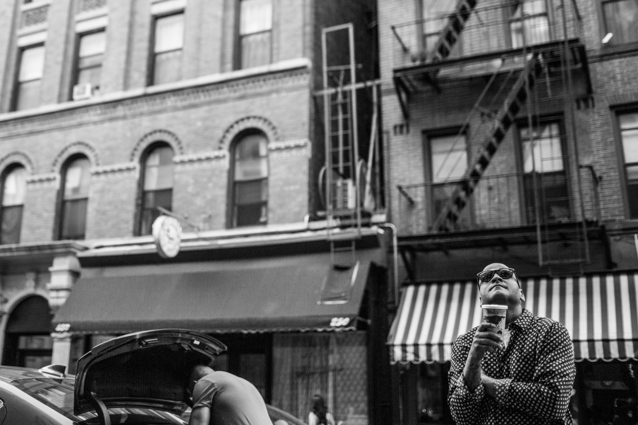  Man with coffee stands amongst buildings in NYC’s lower east side  