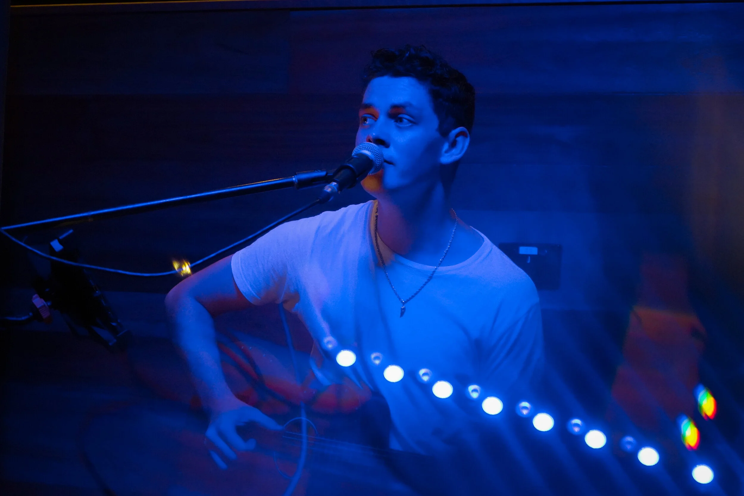Musician singing and playing acoustic guitar with a loop station at a gig playing live music to patrons at a bar