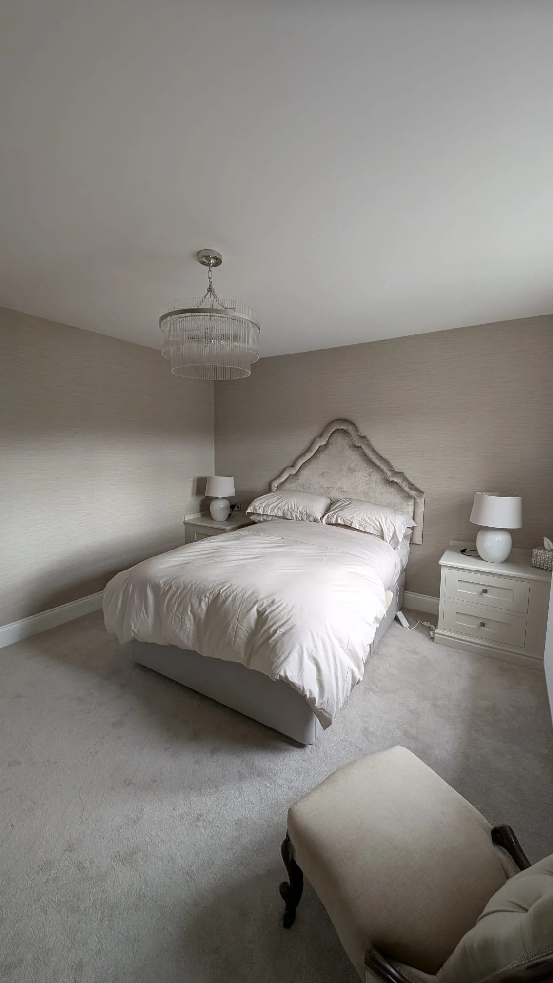 A bedroom with a bed, two nightstands with lamps, an elegant headboard, and cream-colored carpet.
