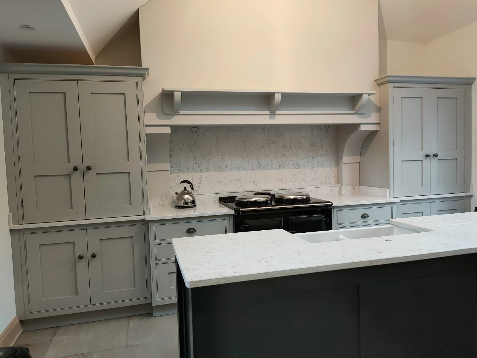 Light gray kitchen with cabinets, marble countertops, a stove, and a kettle.