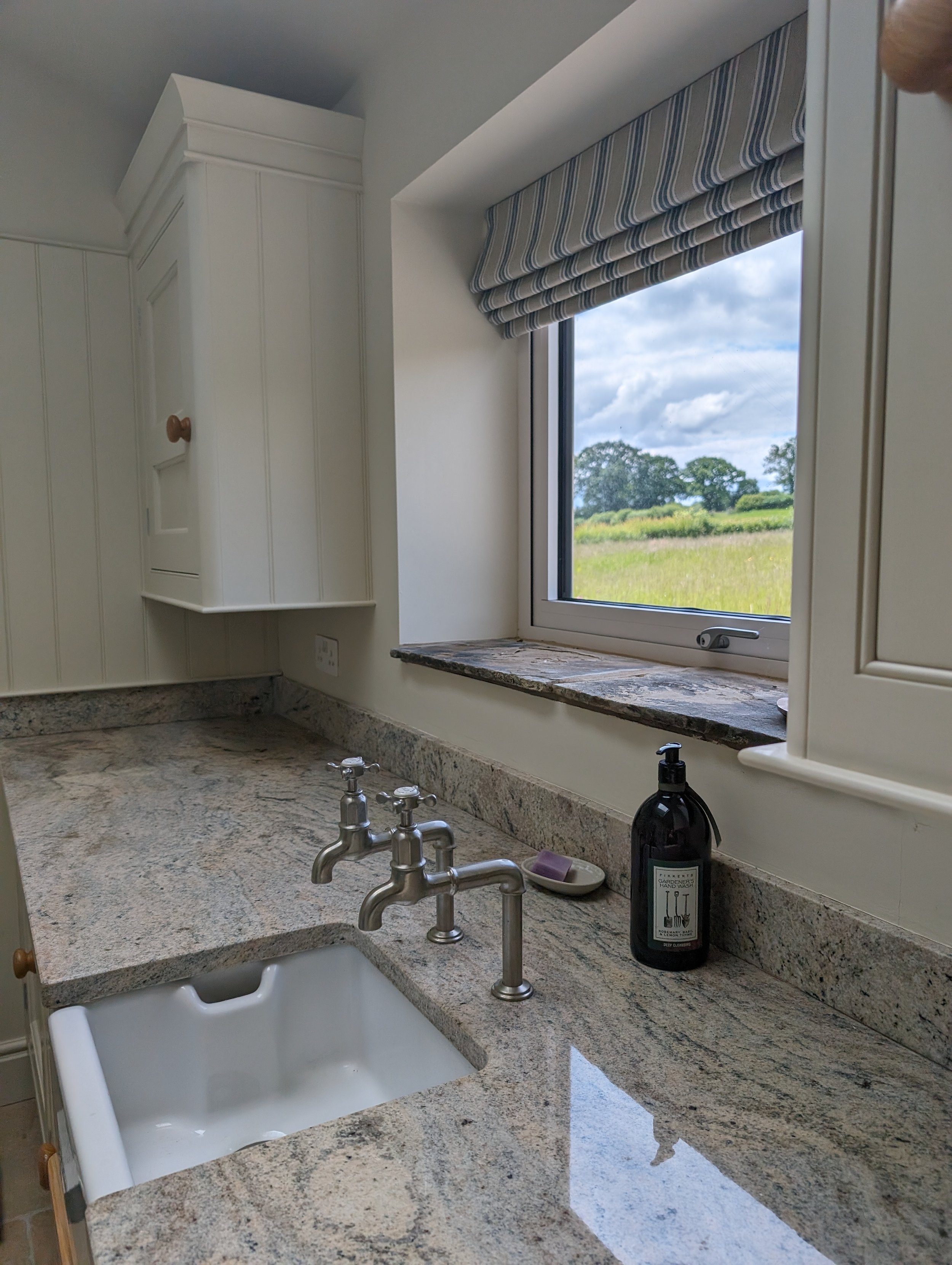 A kitchen countertop with a white farmhouse sink, a soap dispenser, and a window showing a grassy field outside.