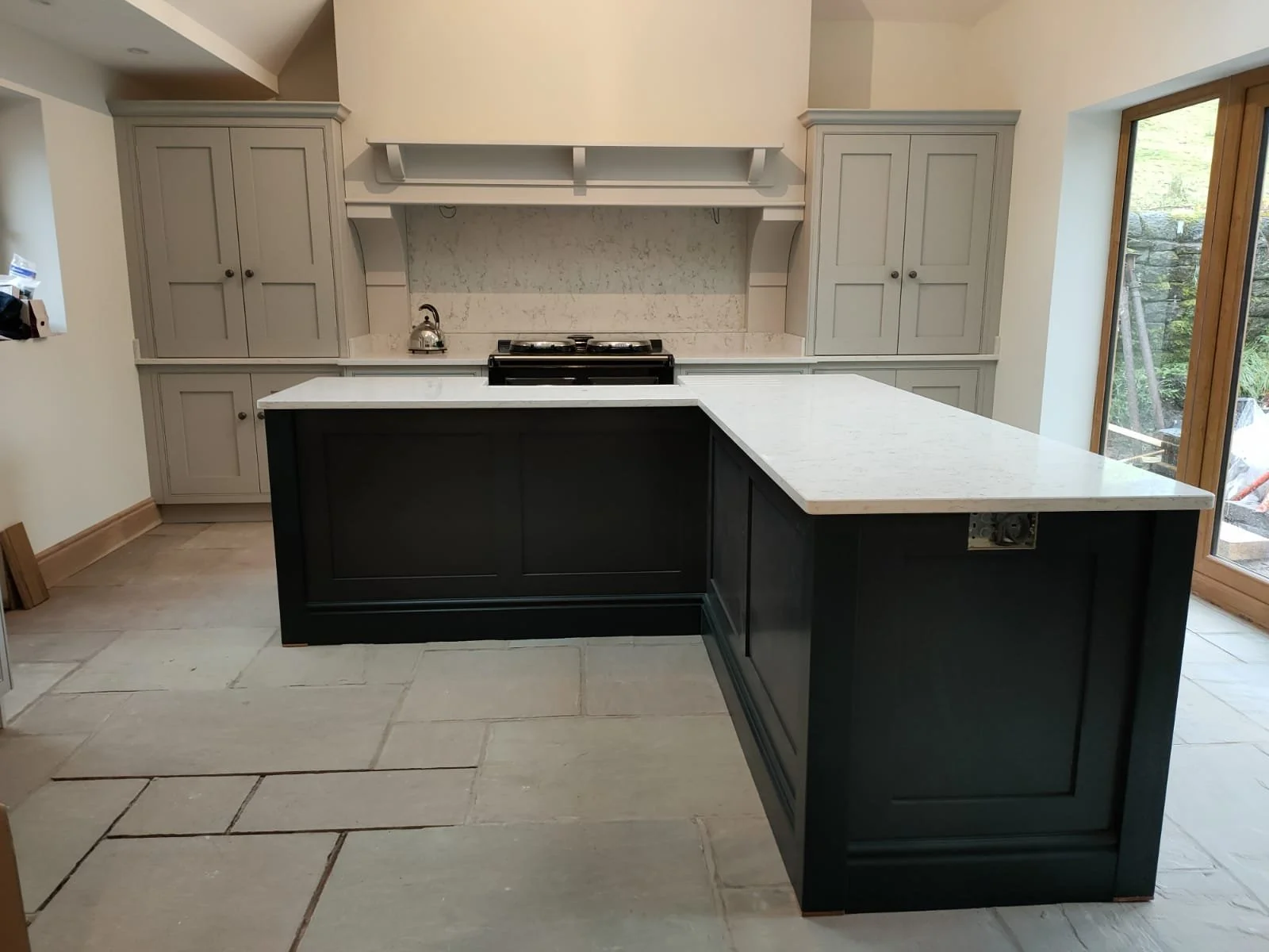 Modern kitchen with gray cabinets and a black kitchen island with white marble countertop, a stove, a teapot, and large sliding glass doors leading outside.
