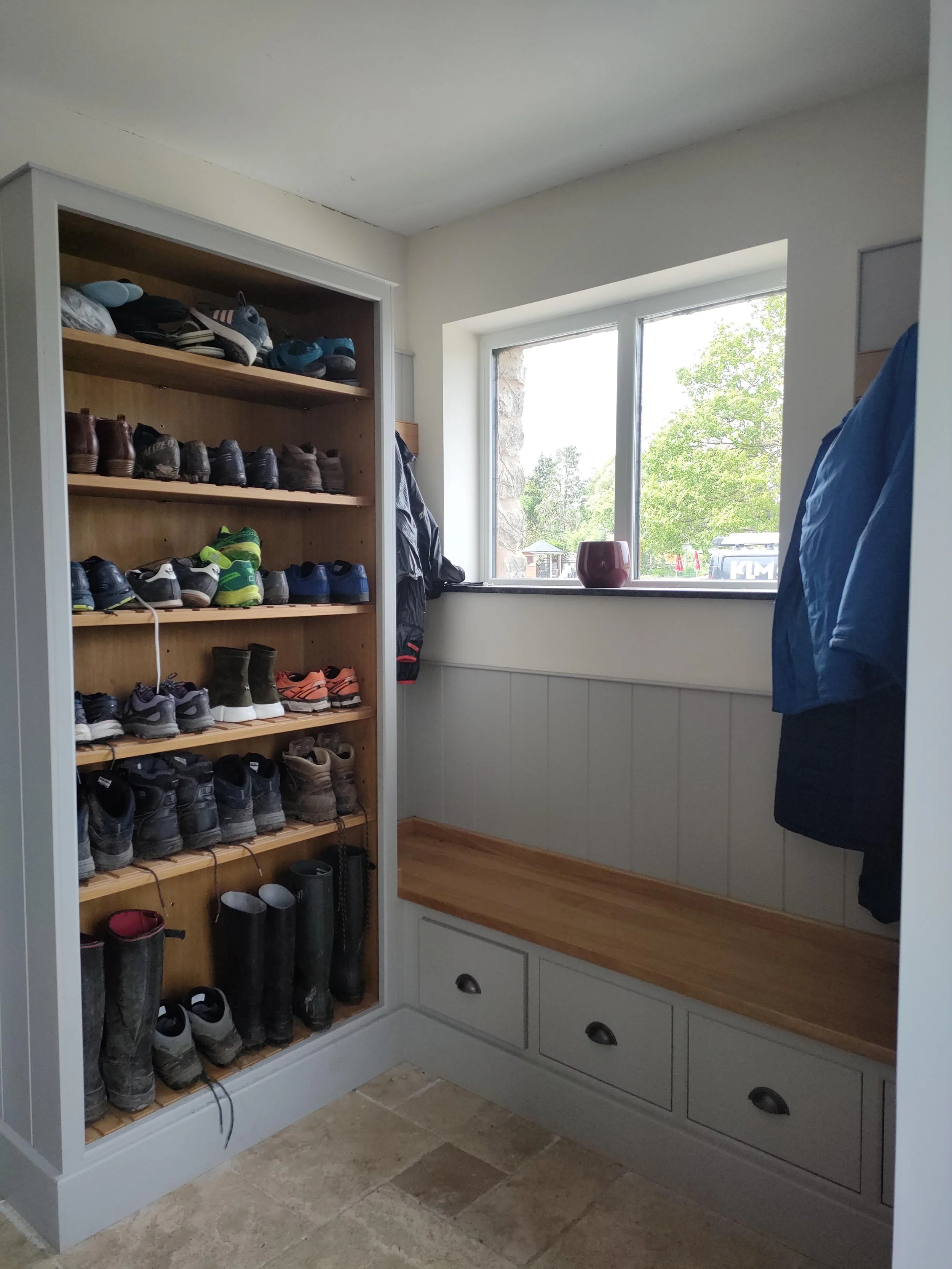 A doorway with a built-in shoe rack filled with various shoes and boots, and a window with a view of trees outside.