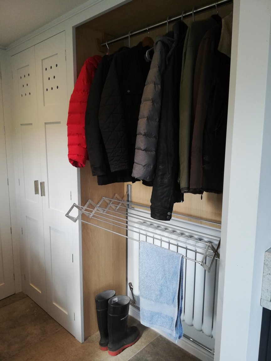Closet with a rod of hanging jackets and coats, a drying rack with a towel, and a pair of black boots on the floor.