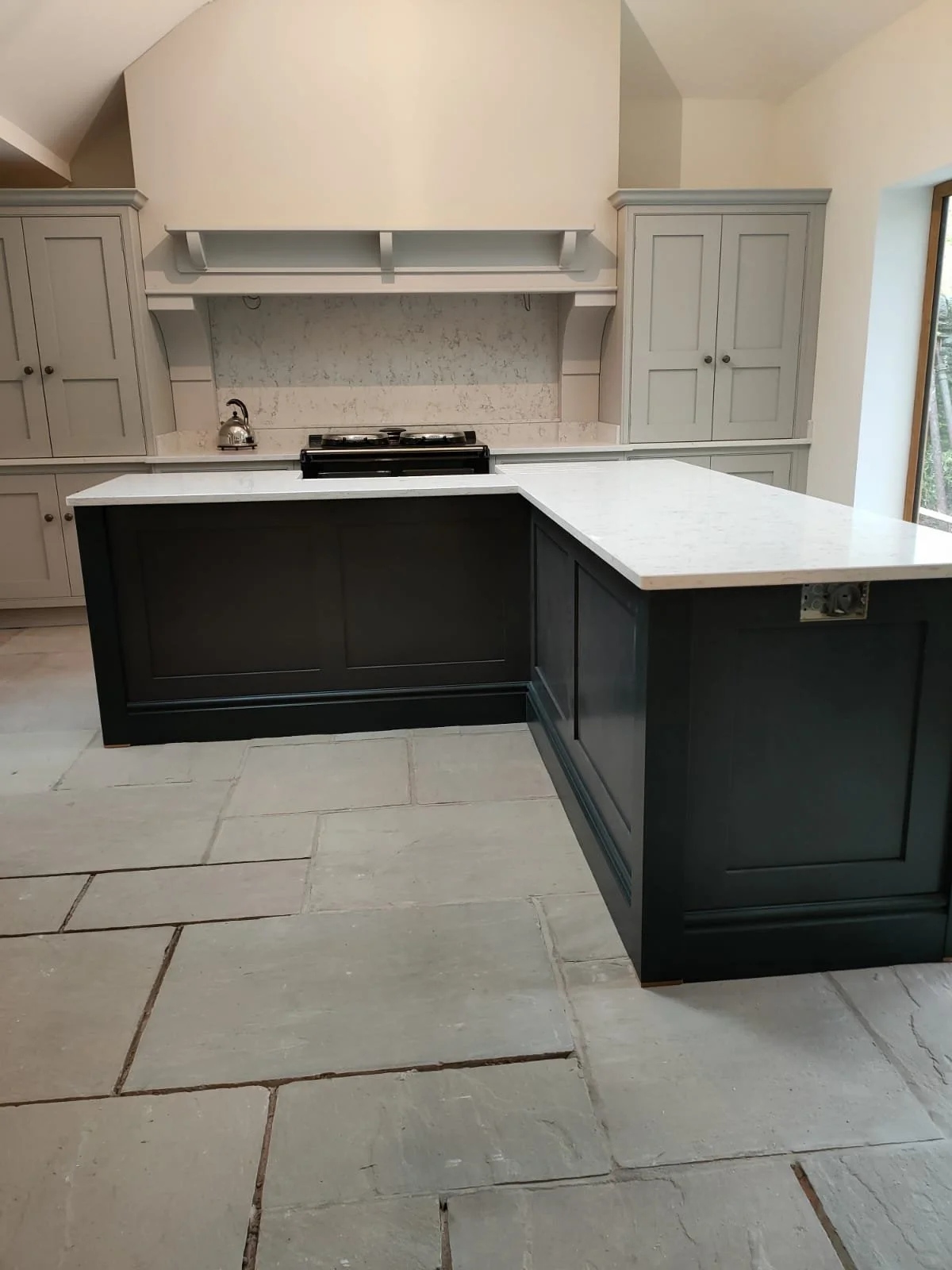 Modern kitchen with a black island, light gray cabinets, white countertops, and beige tile flooring.