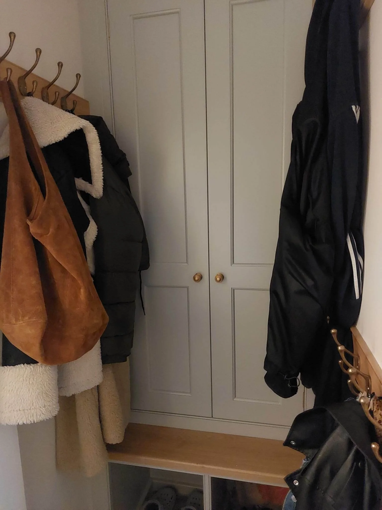 A small entryway with a coat rack holding jackets and bags, a closet with closed double doors, and a wooden shoe rack with some shoes.