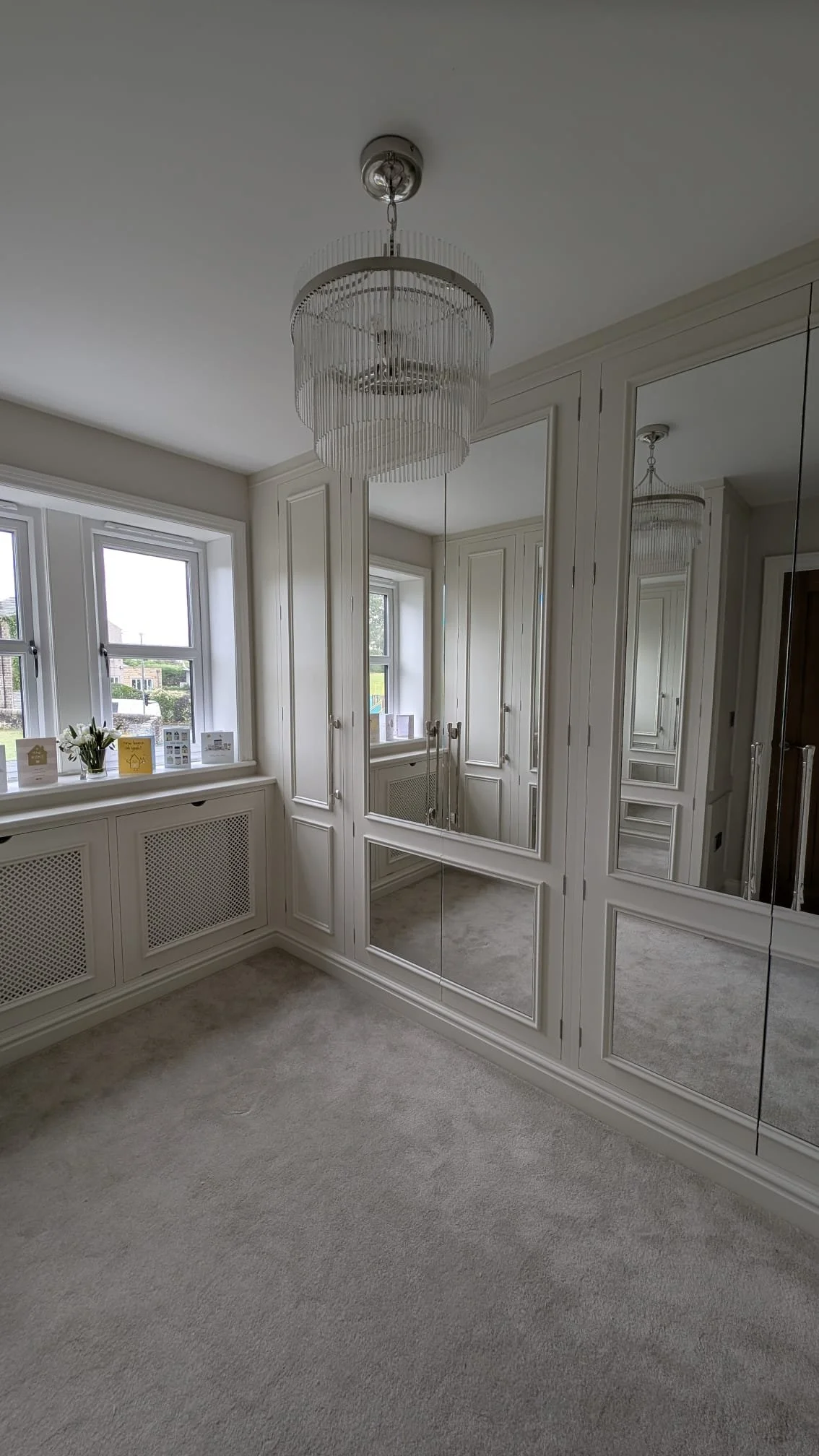 A corner of a room featuring a large mirror closet door, windows with a radiator below, and a chandelier hanging from the ceiling.
