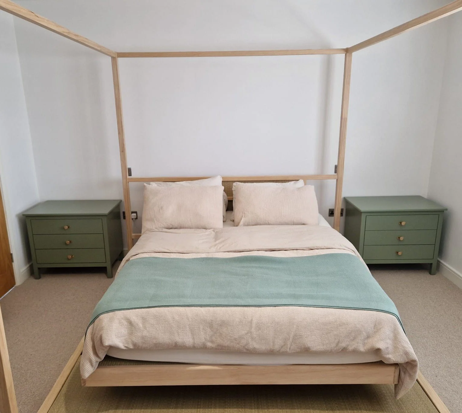 A bedroom with a bed, two green nightstands, and a wooden four-poster frame.