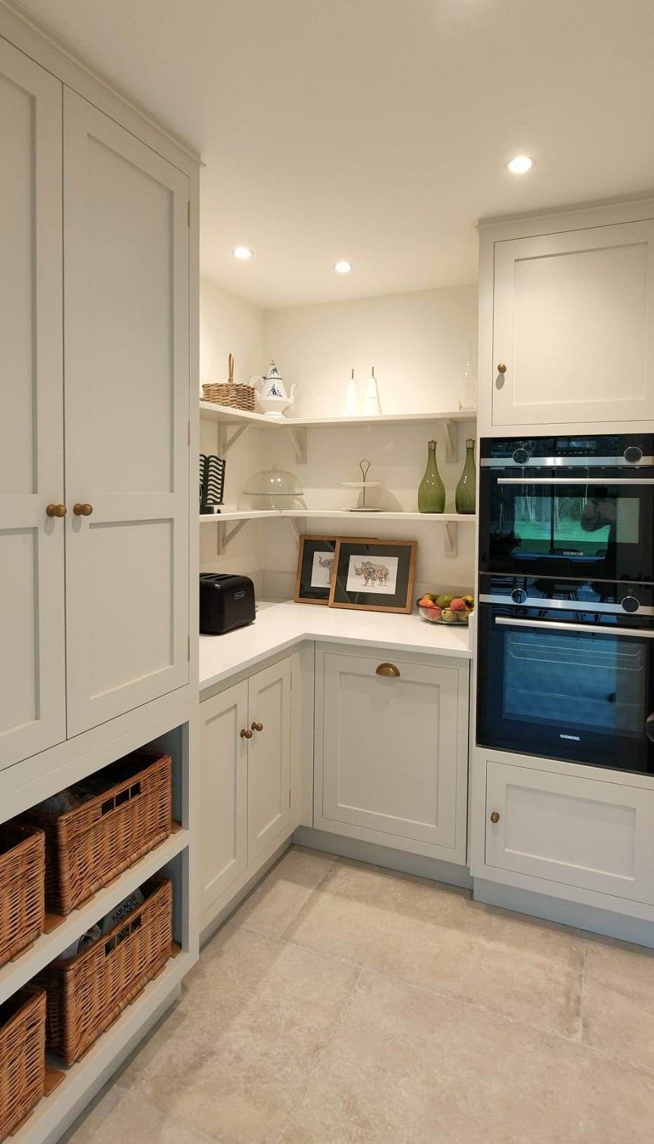 Kitchen with white cabinetry, open shelves, wicker baskets, framed pictures, a bowl of apples, and built-in double oven.