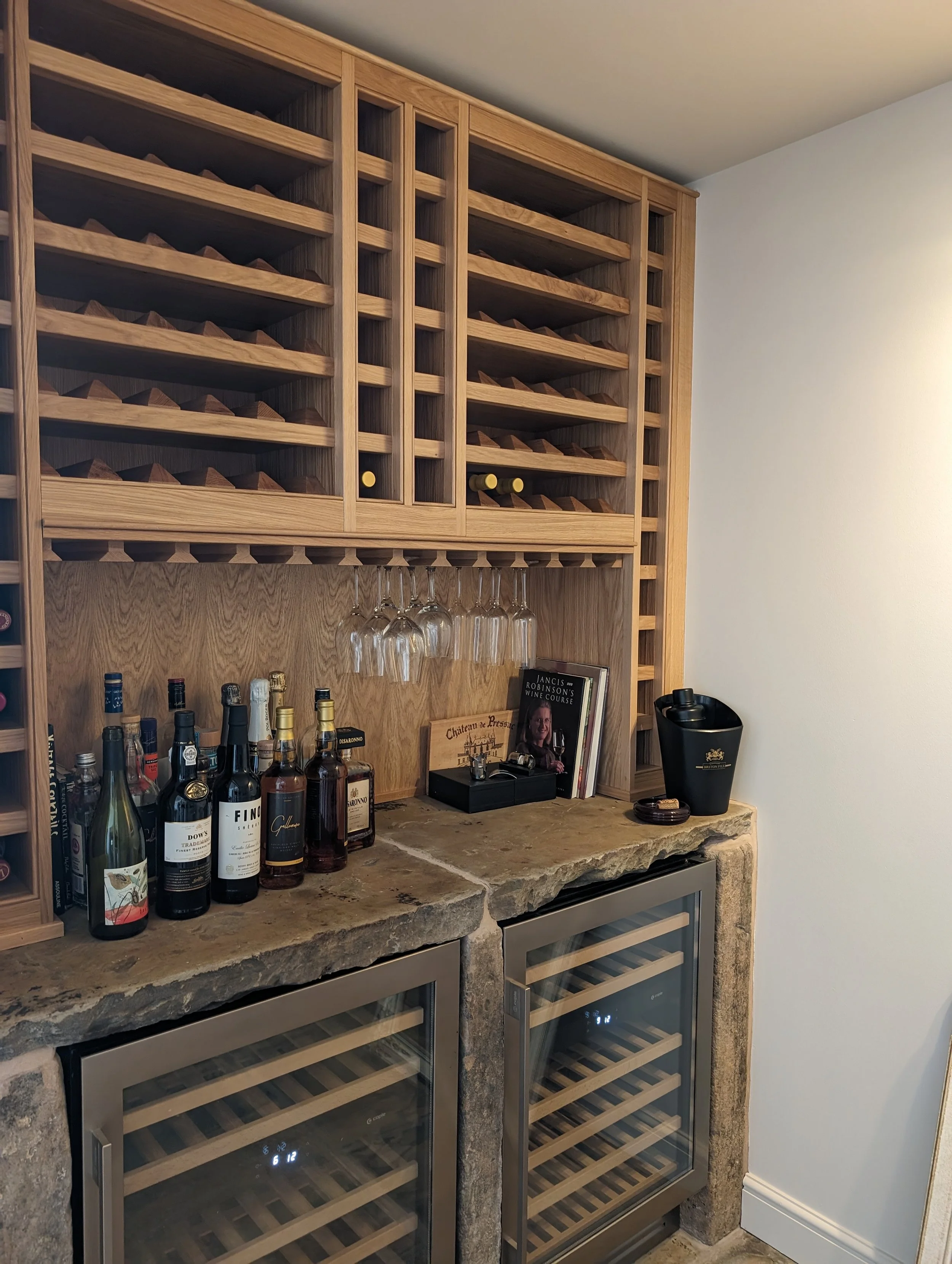 Home bar area with a wooden wine rack, hanging wine glasses, bottles of liquor, a wine cooler, and decorative items.