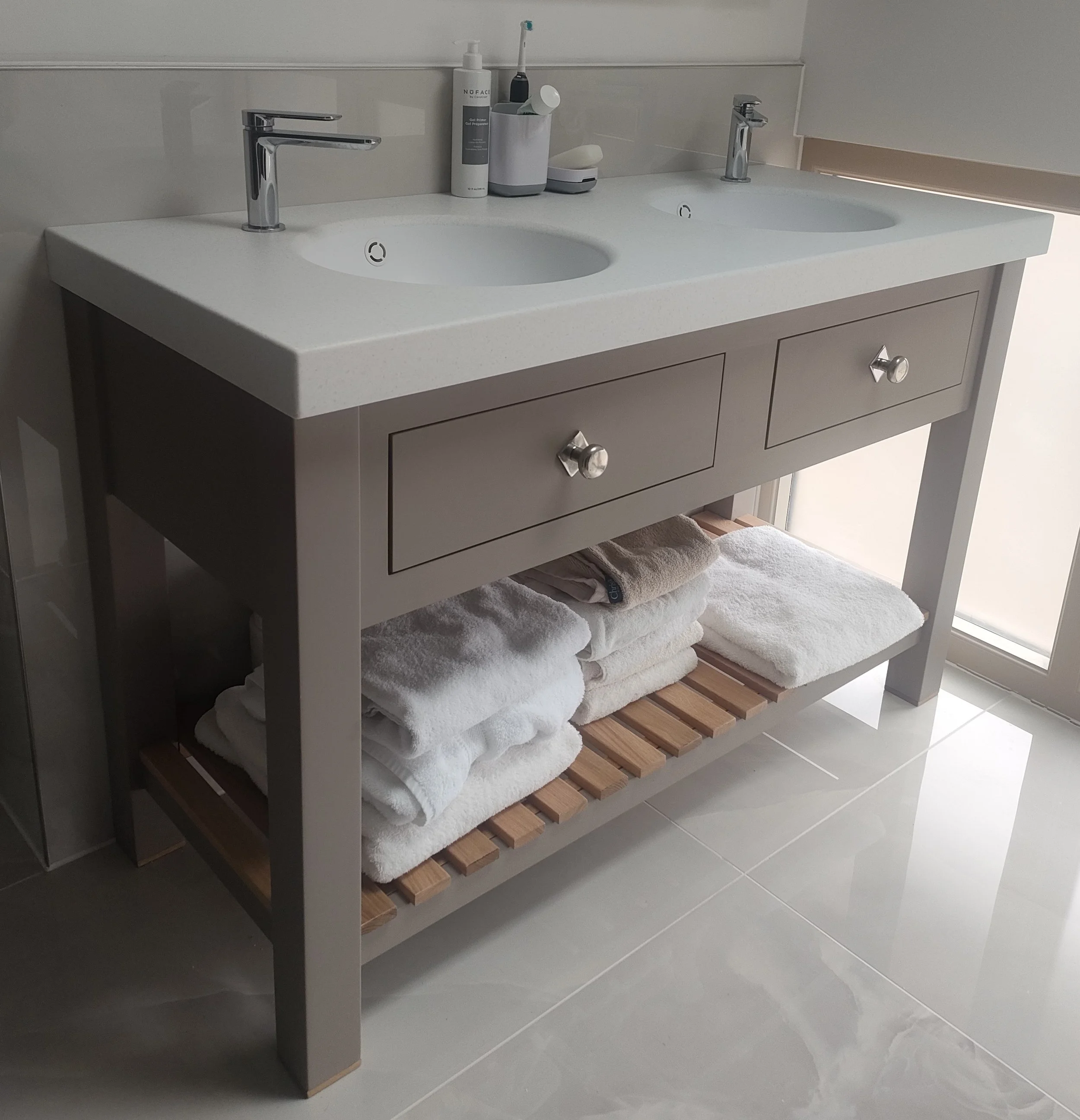 Bathroom vanity with two sinks, storage drawers, and towels underneath. Items on the countertop include soap dispensers and toiletries.