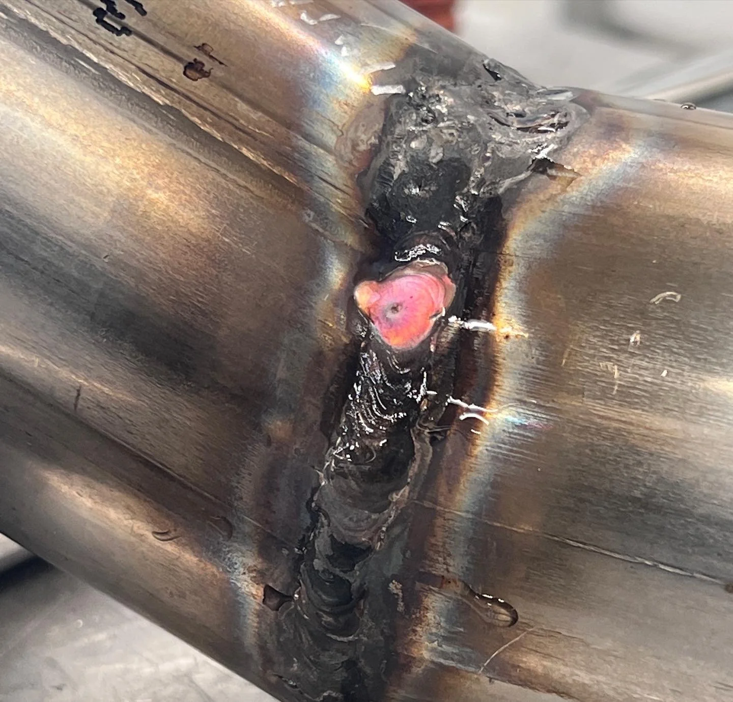 A pink petal weld spot, heat shield color, from TIG welding stainless steel for the exhaust pipe.