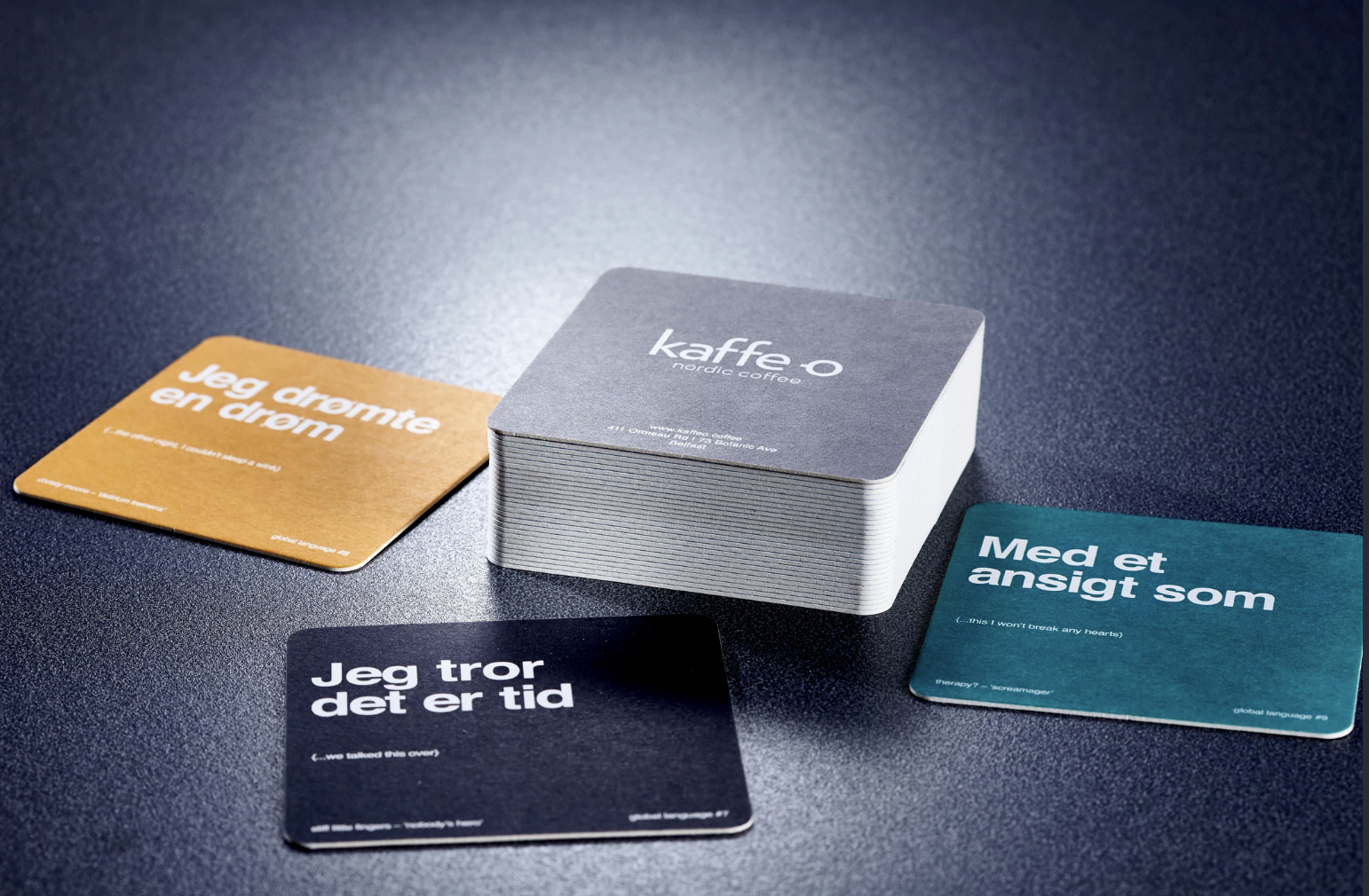 A deck of cards labeled 'kaffe o' with three individual cards around it, each containing text in Scandinavian languages.