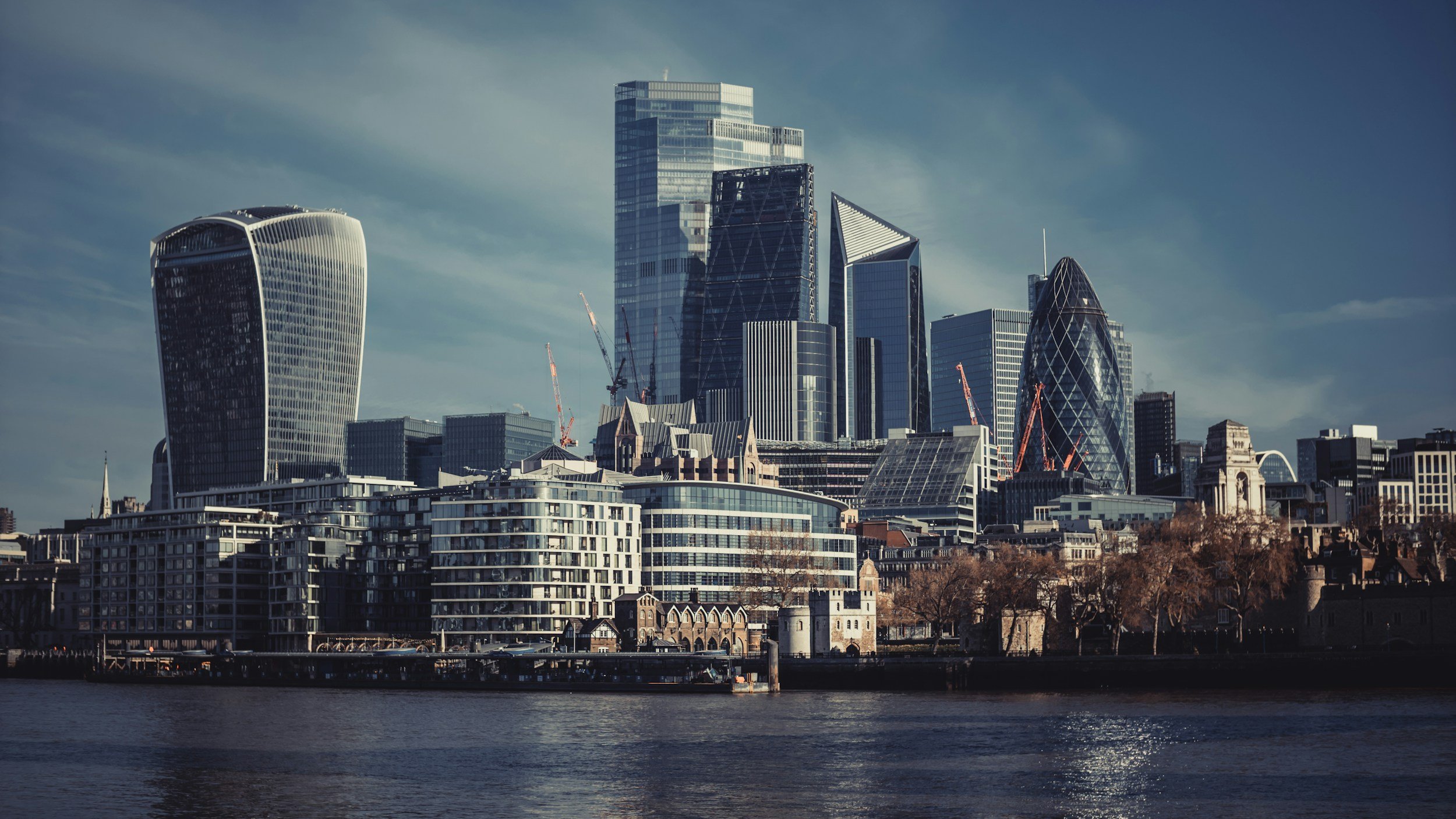 London skyline with modern skyscrapers near the River Thames under a partly cloudy sky.