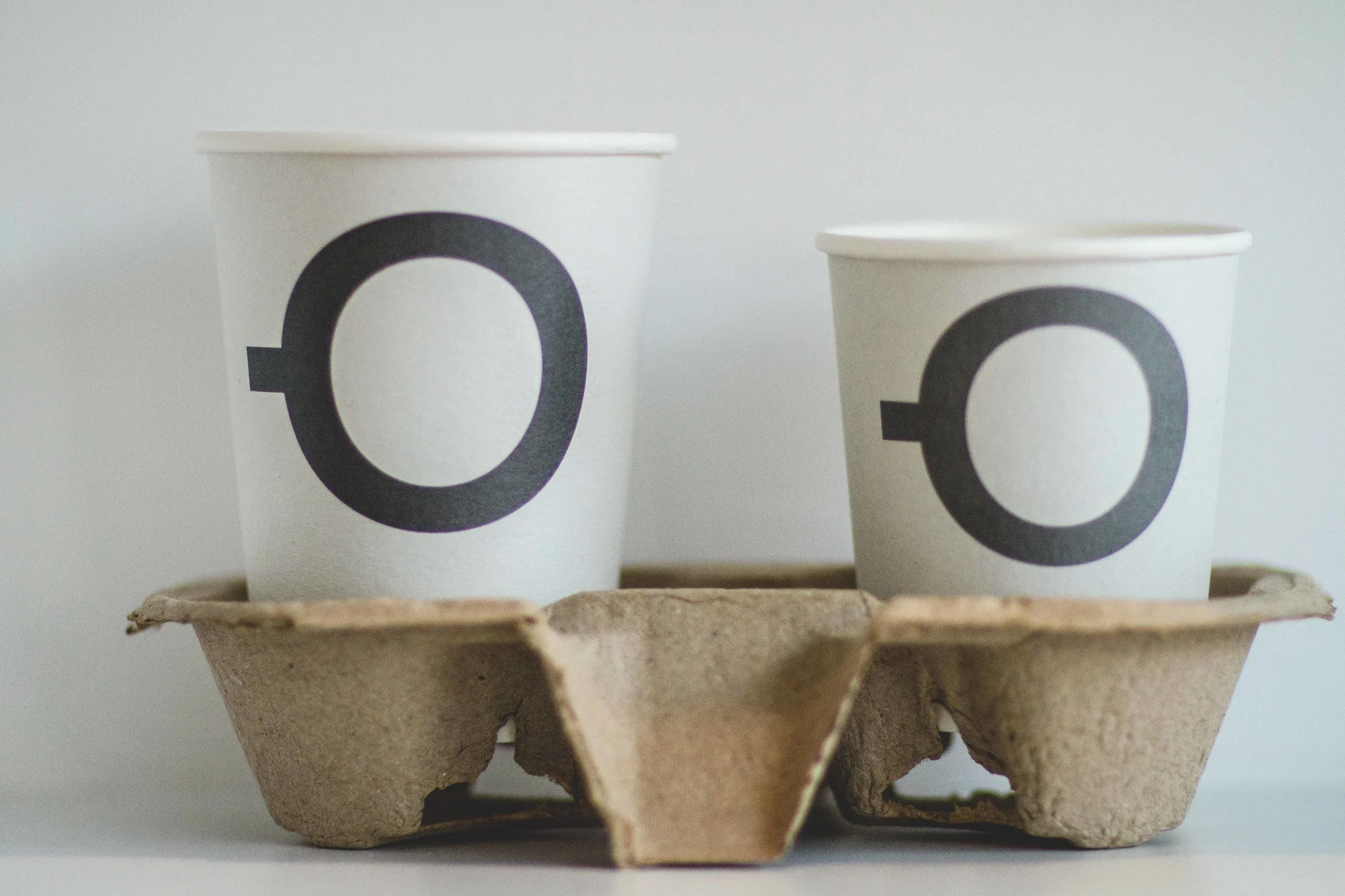 Two white paper cups with black Olympic symbols on them placed inside a cardboard tray on a white background.