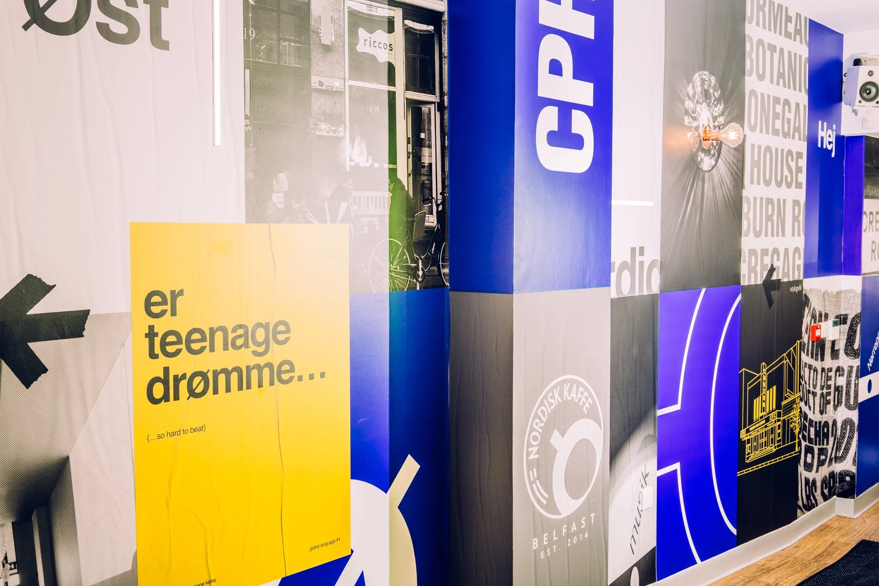 A wall decorated with various colorful posters and graphics, including words like 'Cognition' and 'teenage dreams,' along with logos and illustrations.
