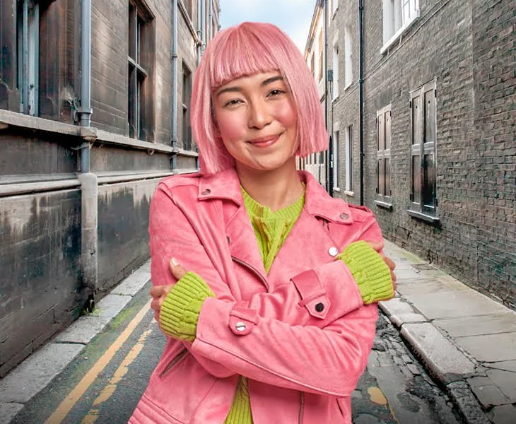 Smiling woman in pink coat with pink hair hugs herself to 'embrace equity for IWD'