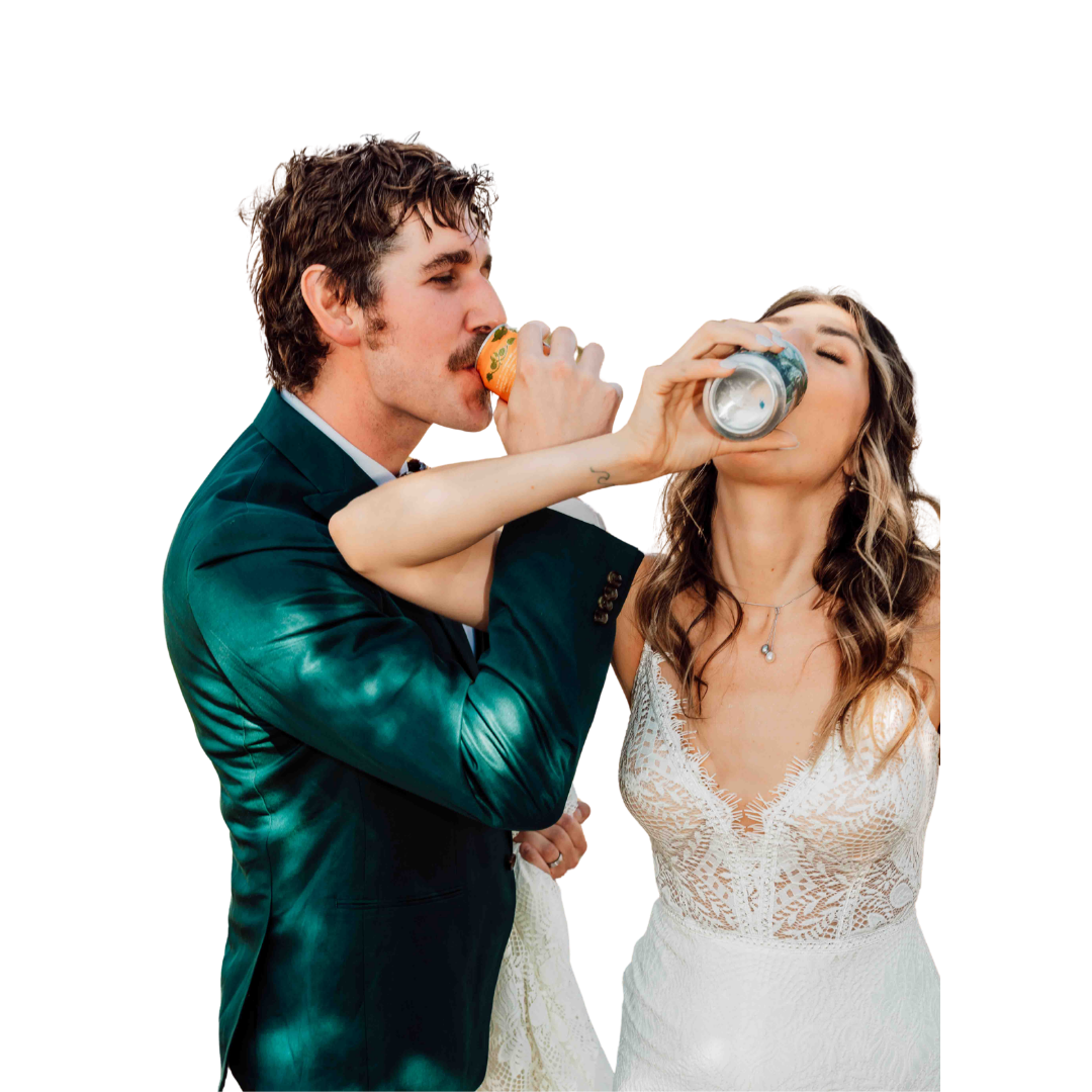 A man in a formal suit is drinking a canned beverage while a woman in a white lace dress is drinking from a glass bottle, with the man's hand supporting the bottle to her lips.