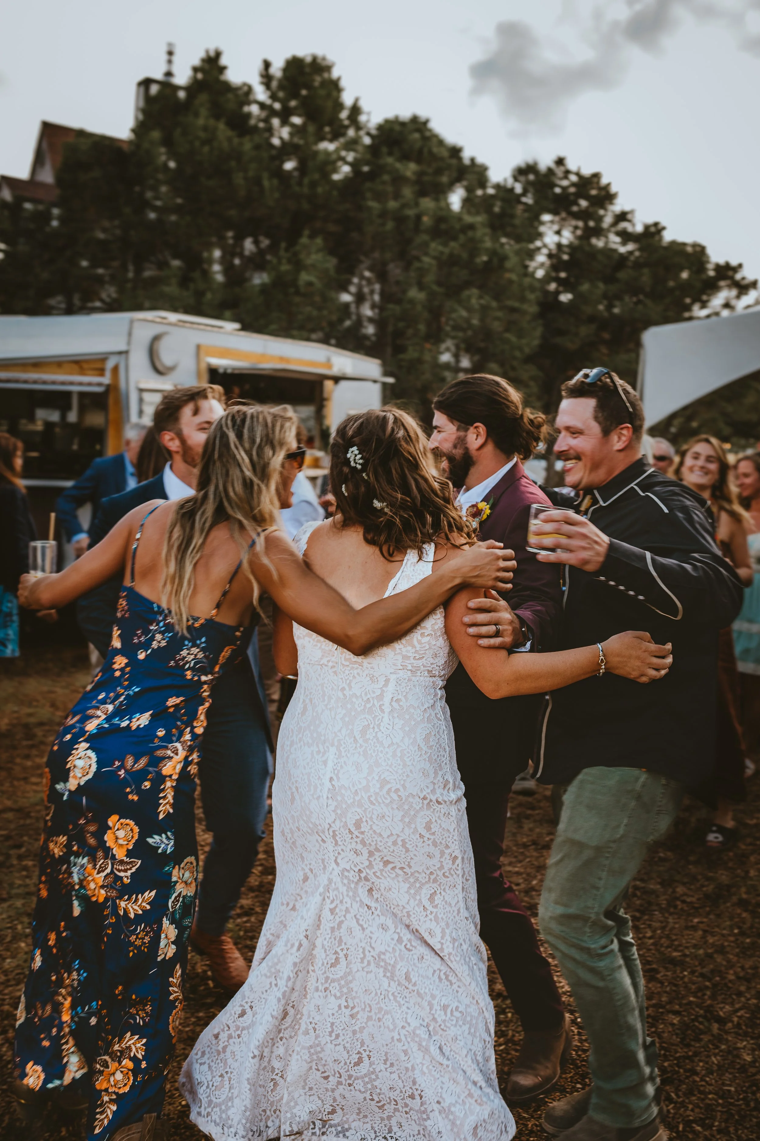 Wedding couple getting hugged from a bunch of friends. Drinks in hand Blue Coyote Ranch in Salida, CO.