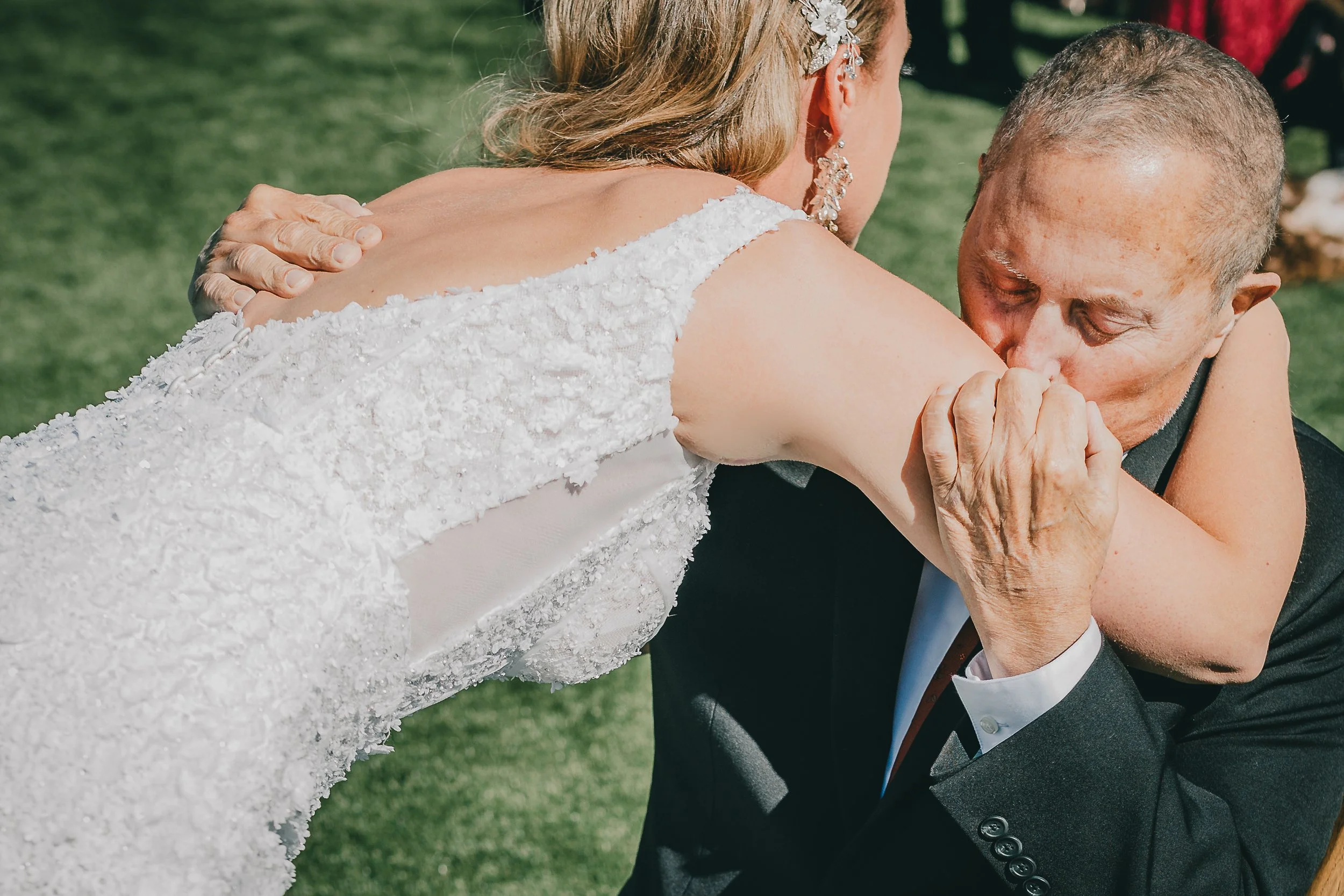 Very ill father kissing his daughter on the shoulder while she hugs him during their first look.
